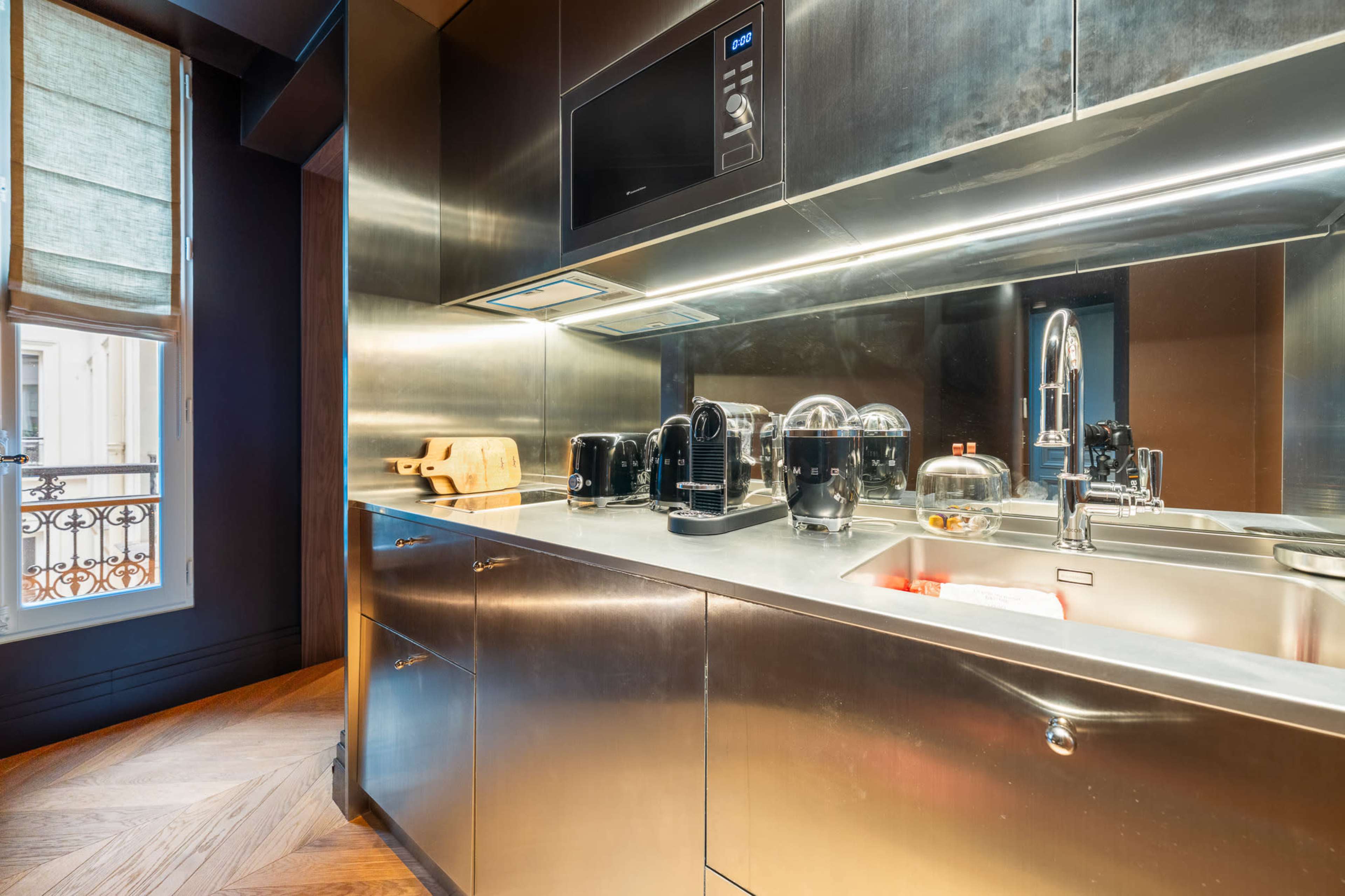 The image shows a modern kitchen with stainless steel surfaces, a microwave, and various small appliances arranged on the countertop.