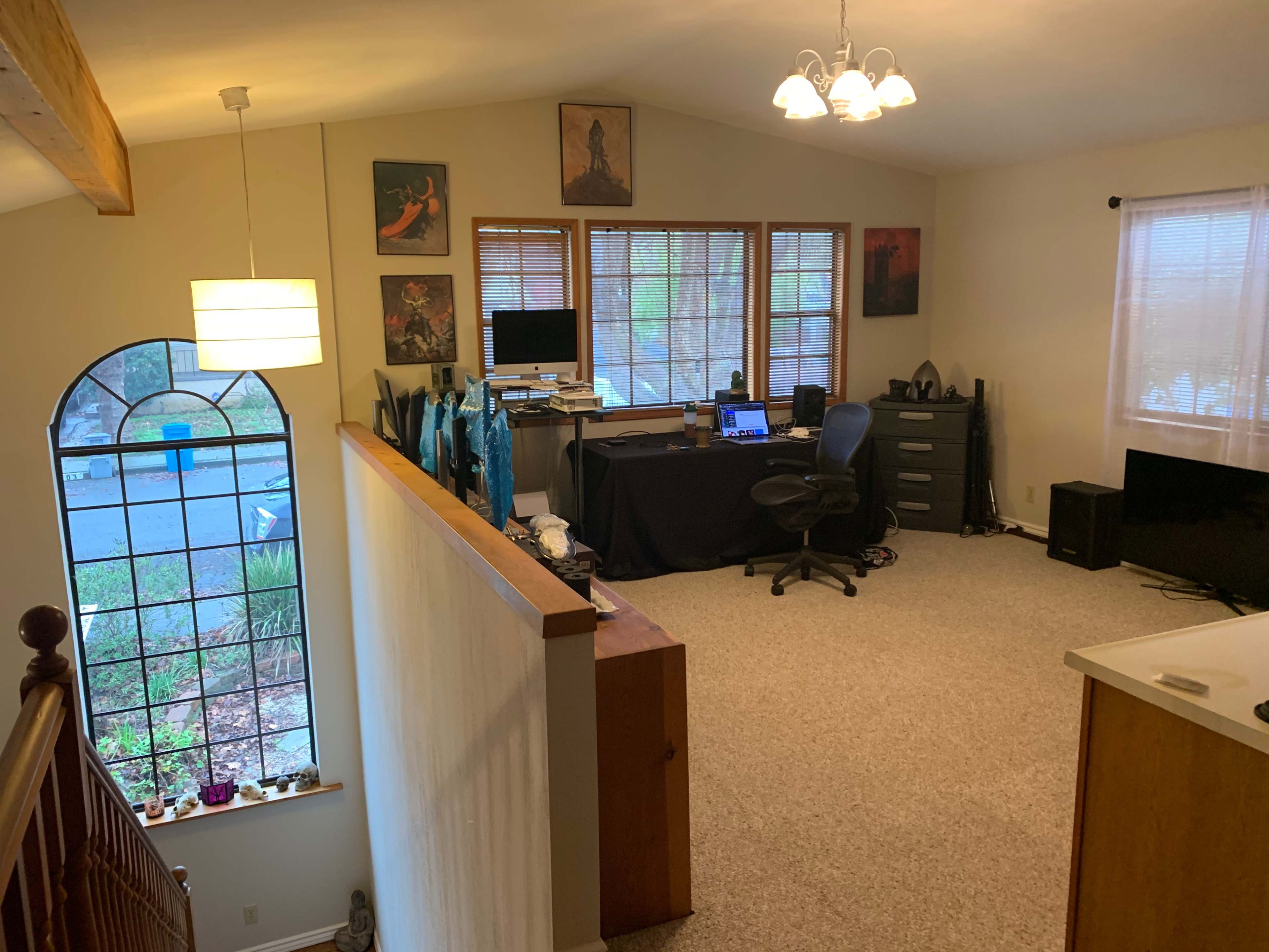 The image shows a home office area with a desk and computer, located in a well-lit room with carpeted flooring and several wall decorations.