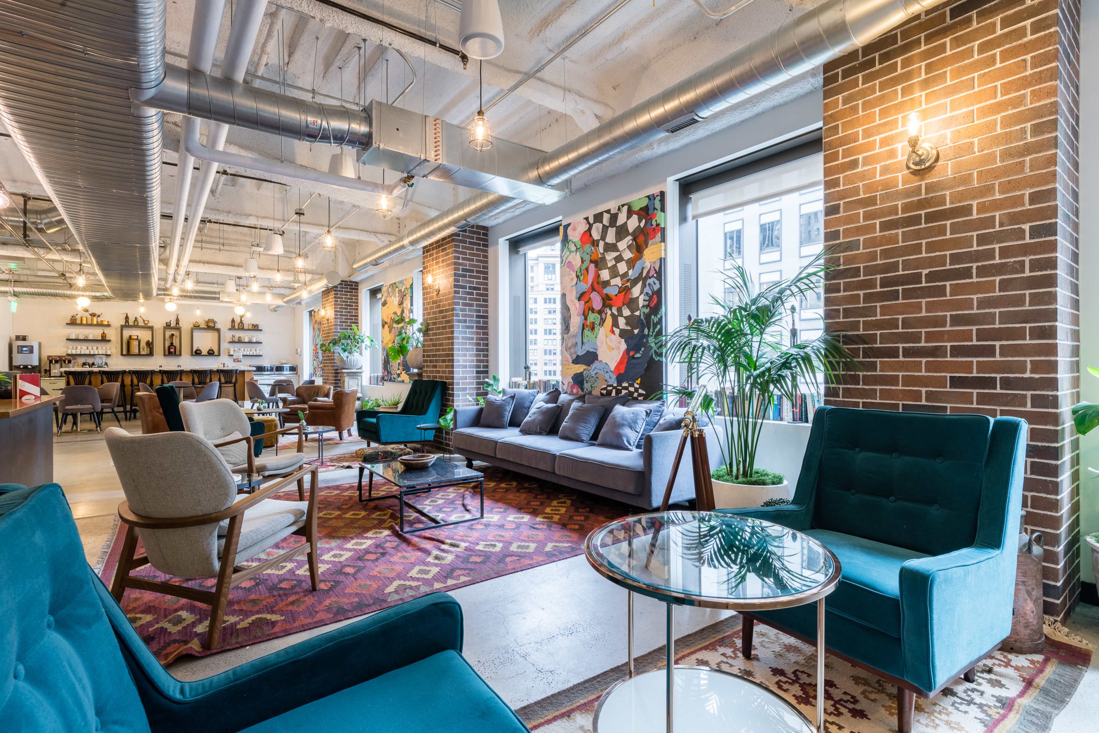 A modern, open-concept lounge area featuring comfortable seating, a patterned rug, and decorative plants amidst exposed brick walls.