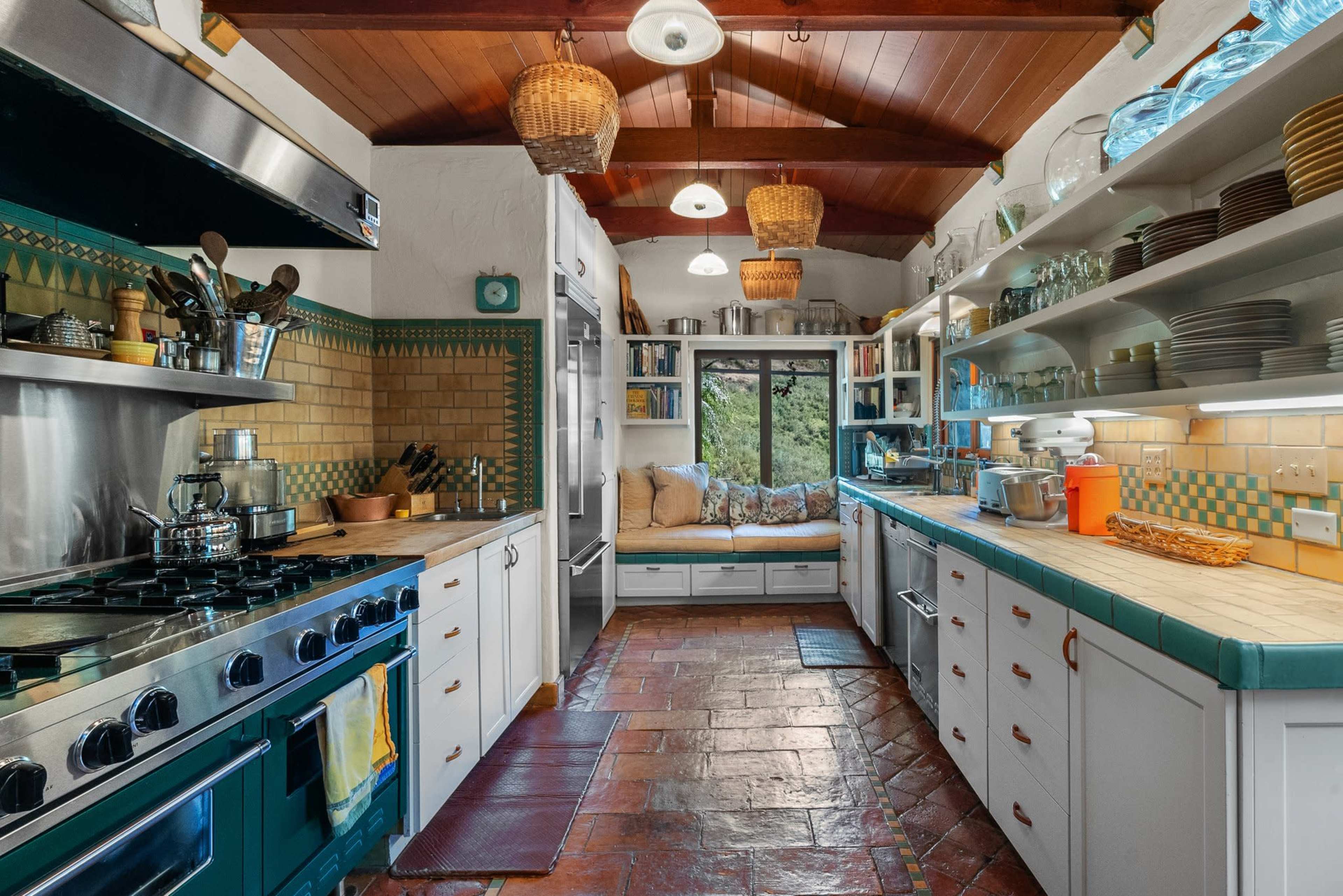 The kitchen features a central island, stainless steel appliances, white cabinetry, and a bright window nook with cushions, all accented by colorful tiles.