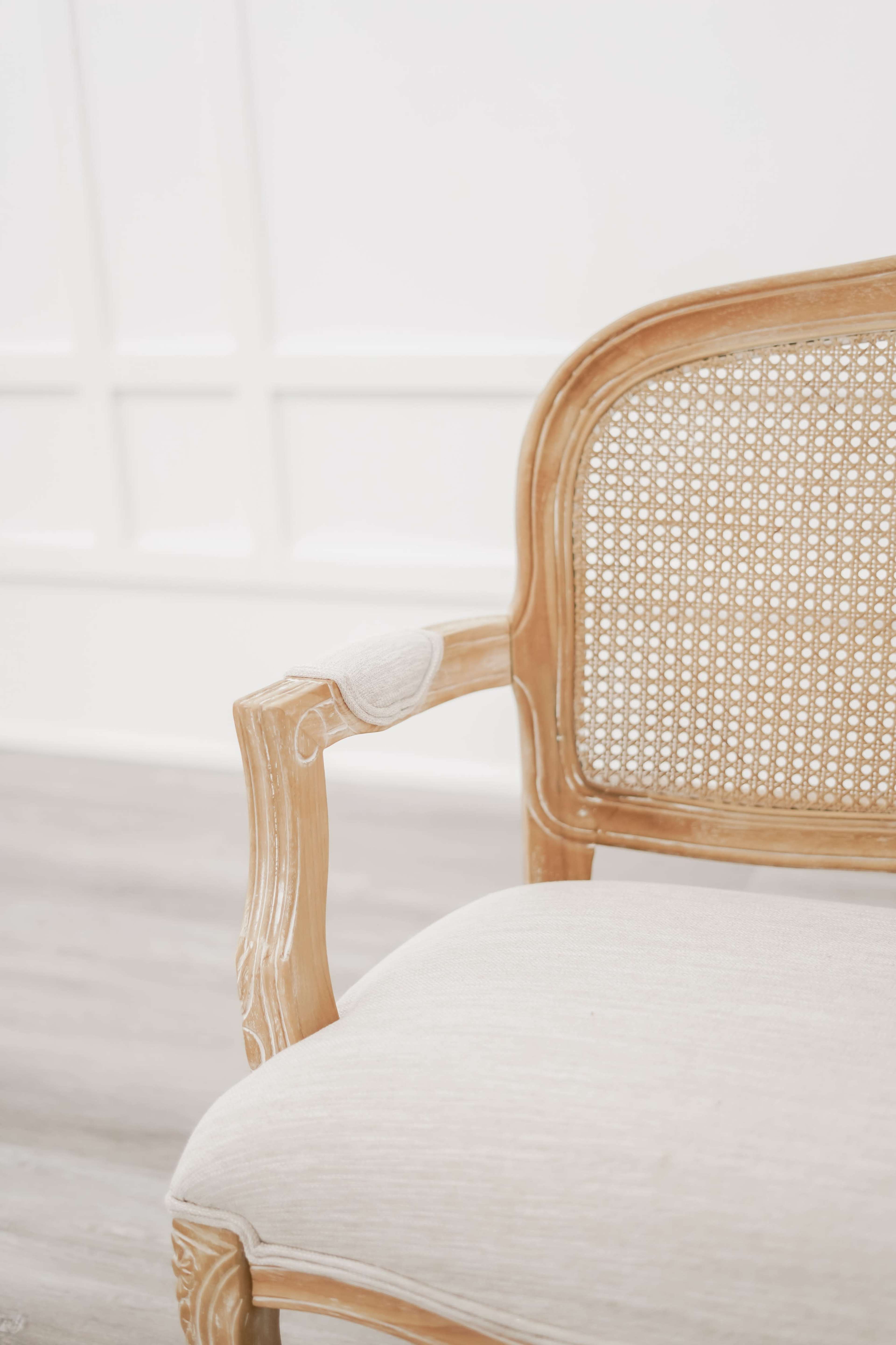 A wooden chair with a caned backrest and upholstered seat is positioned in a bright, minimalistic room.
