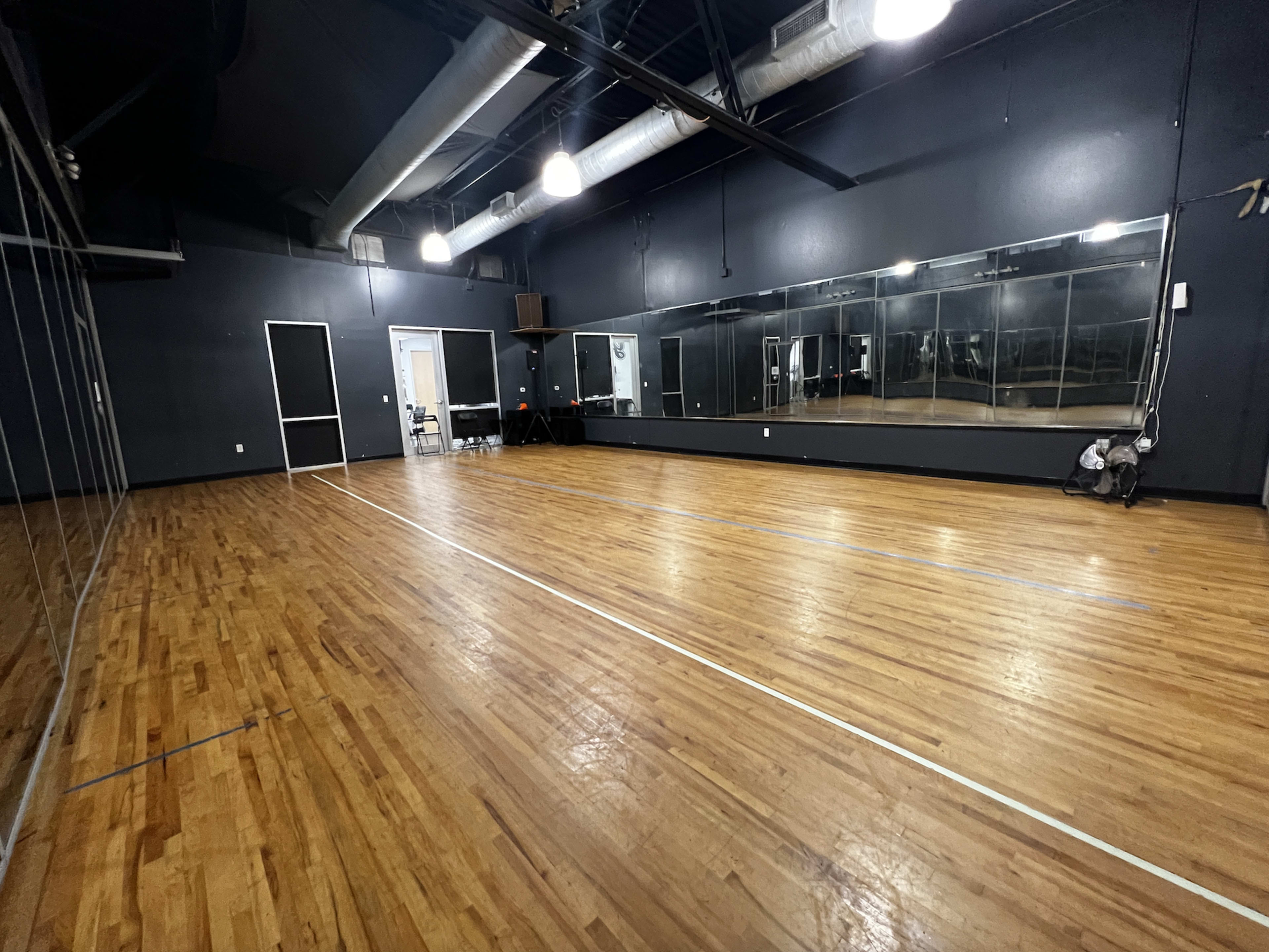 A spacious dance studio with hardwood flooring, mirrored walls, and overhead lighting.