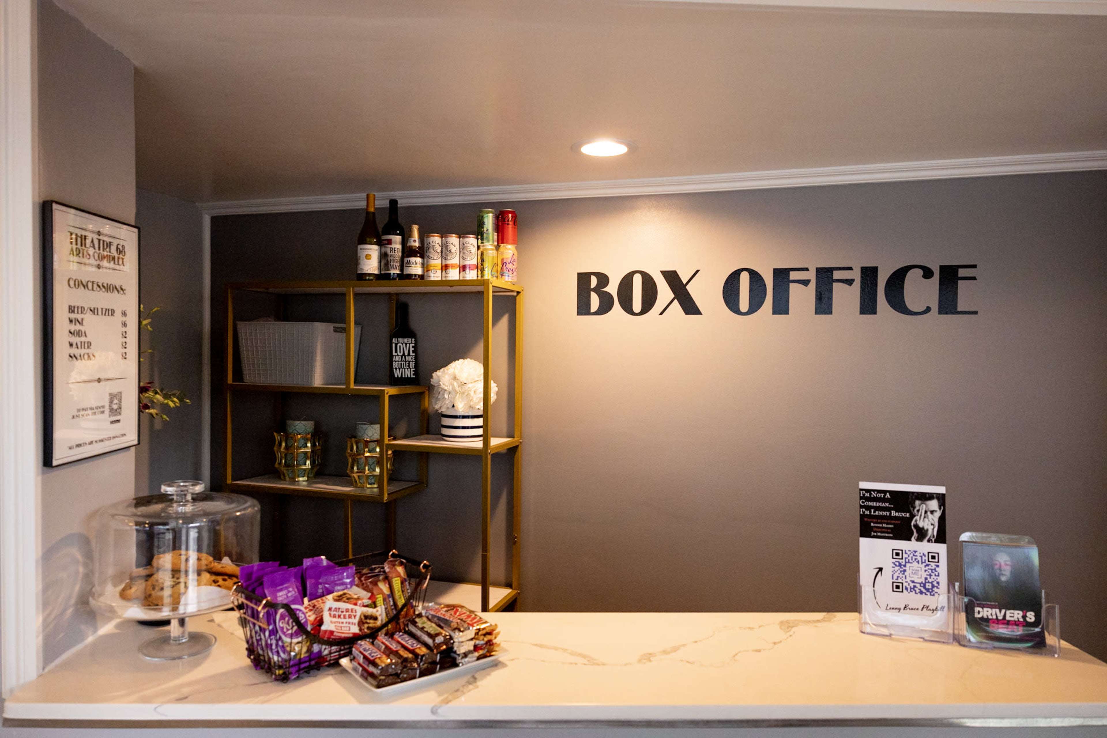 A box office area with a display of snacks, drinks, and decorations on shelves against a gray wall.