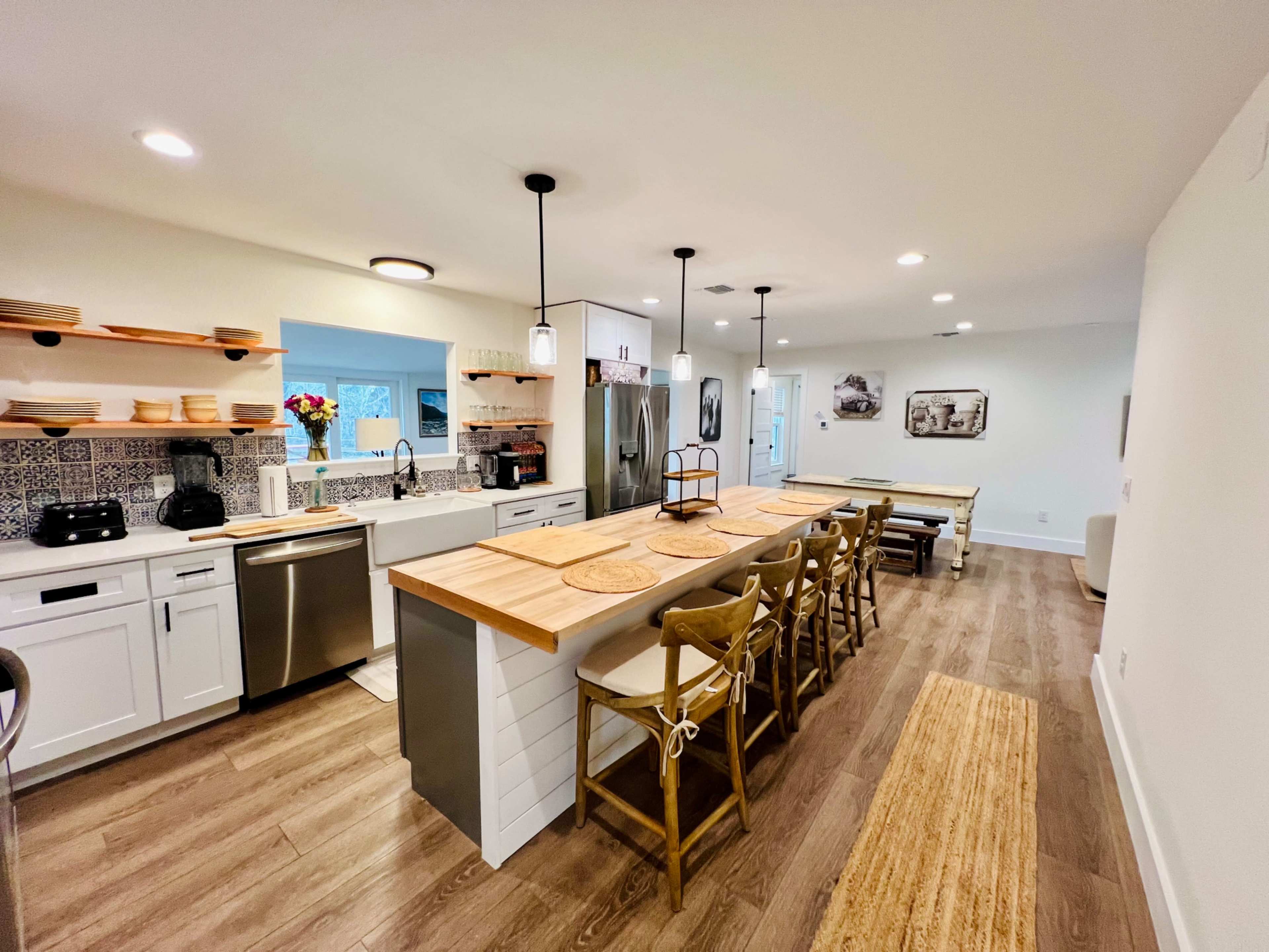 A modern kitchen features white cabinetry, a large wooden island with seating, and an adjacent dining area with a long table.