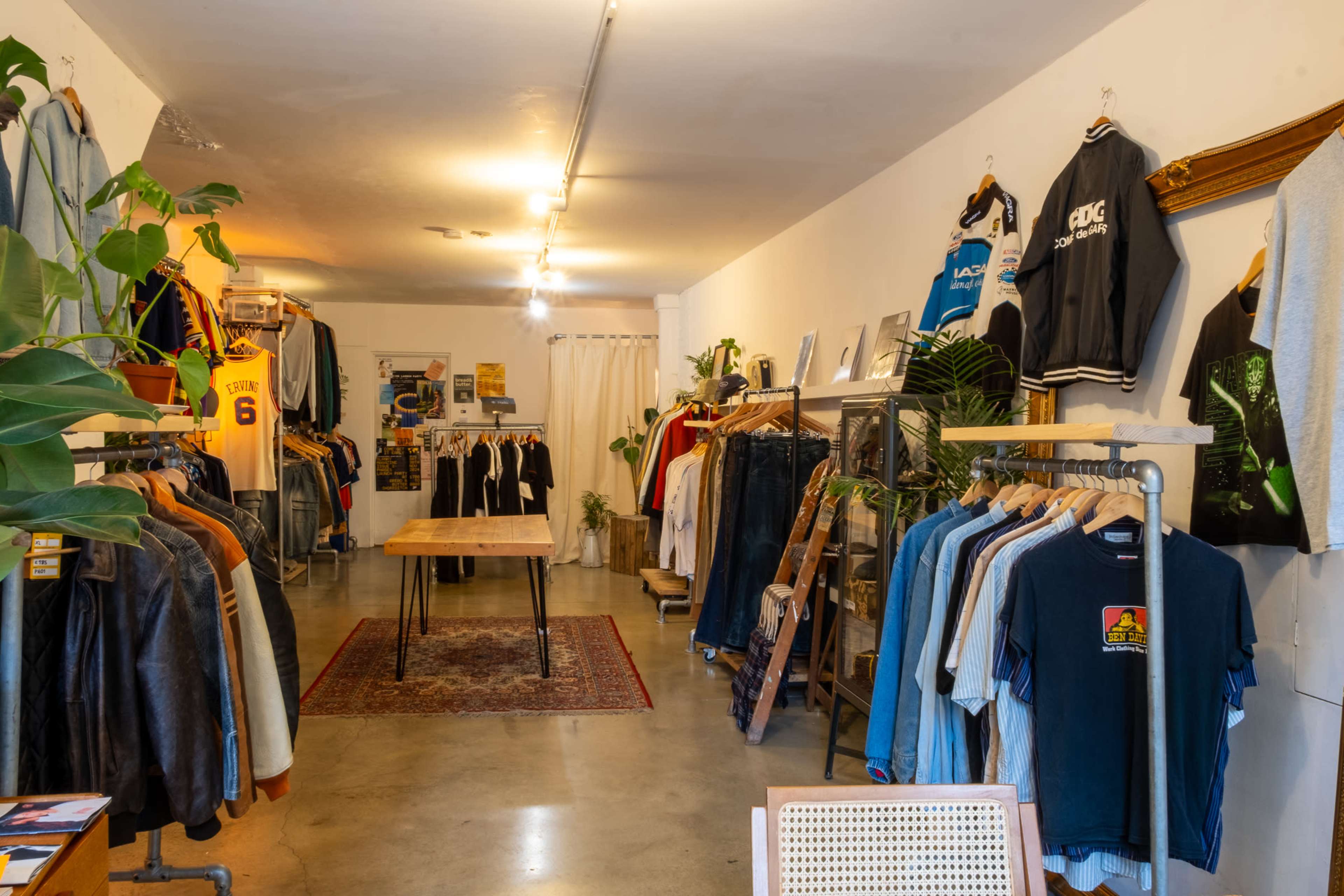 The image shows the interior of a clothing boutique featuring racks of vintage apparel and a wooden table in a well-lit space.