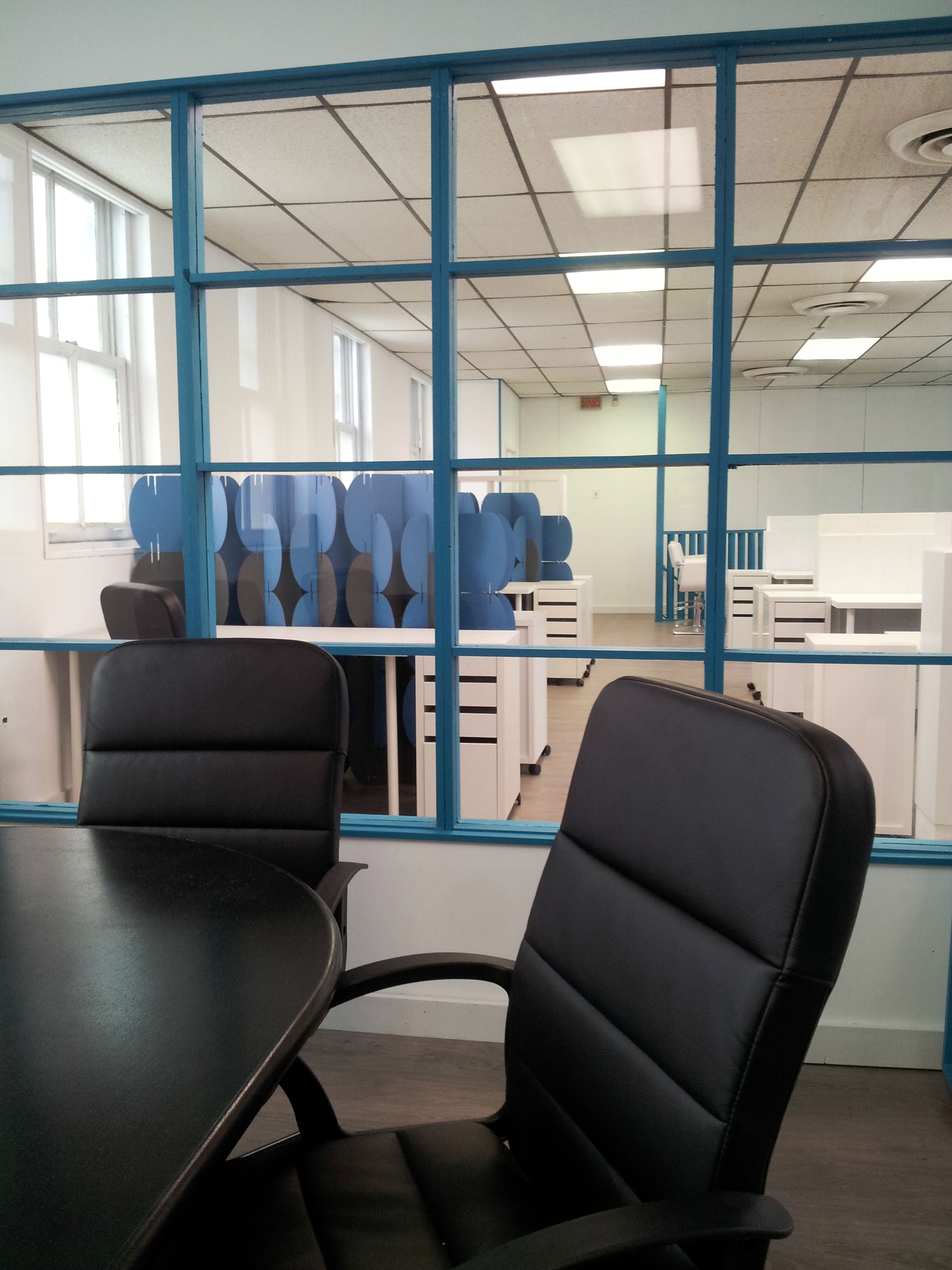 A modern office space with blue accents, featuring several empty desks and chairs visible through a large window.