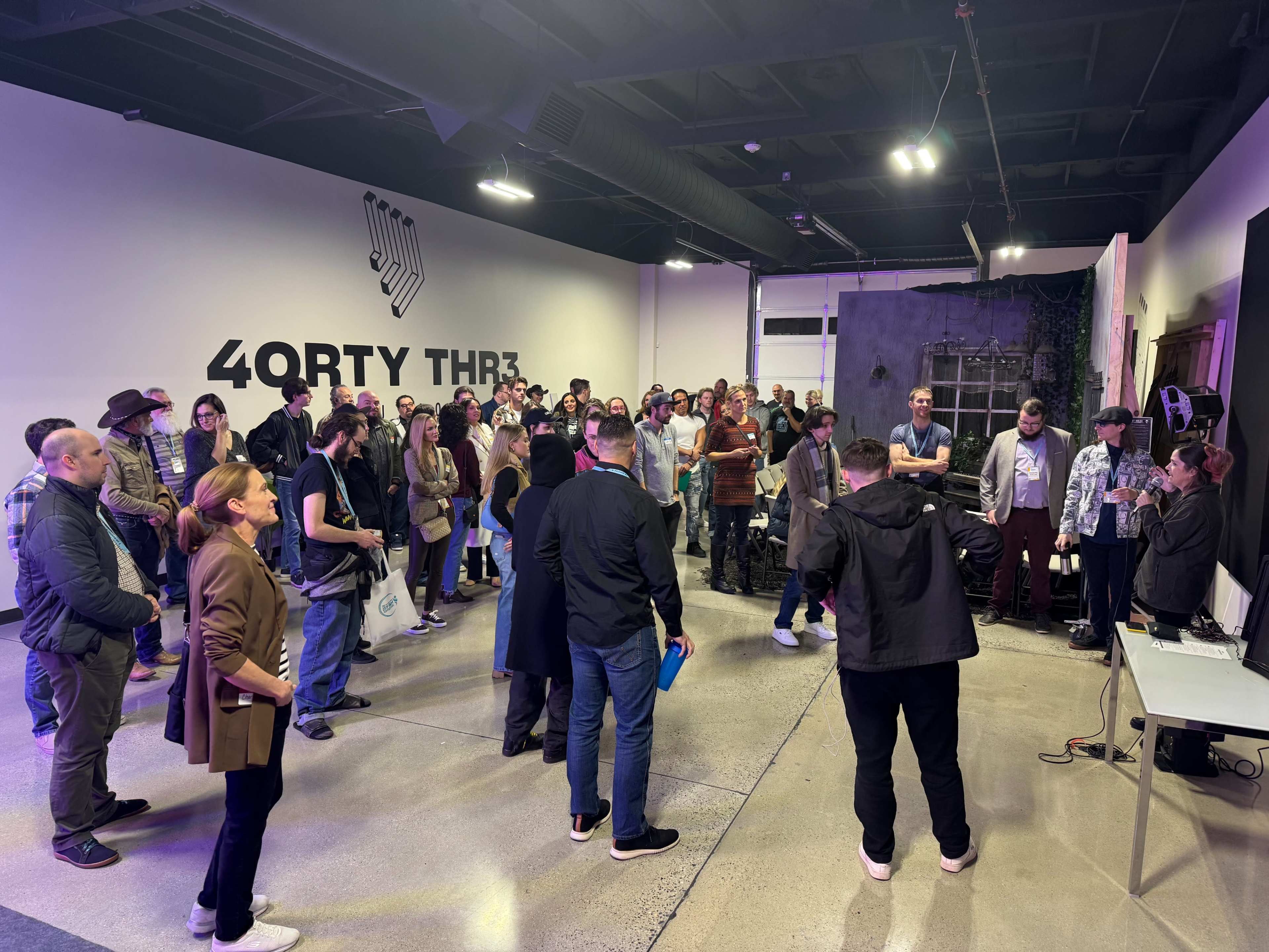 A crowd of people gathers in a brightly lit indoor space for an event, with some individuals standing in front of a presentation area.