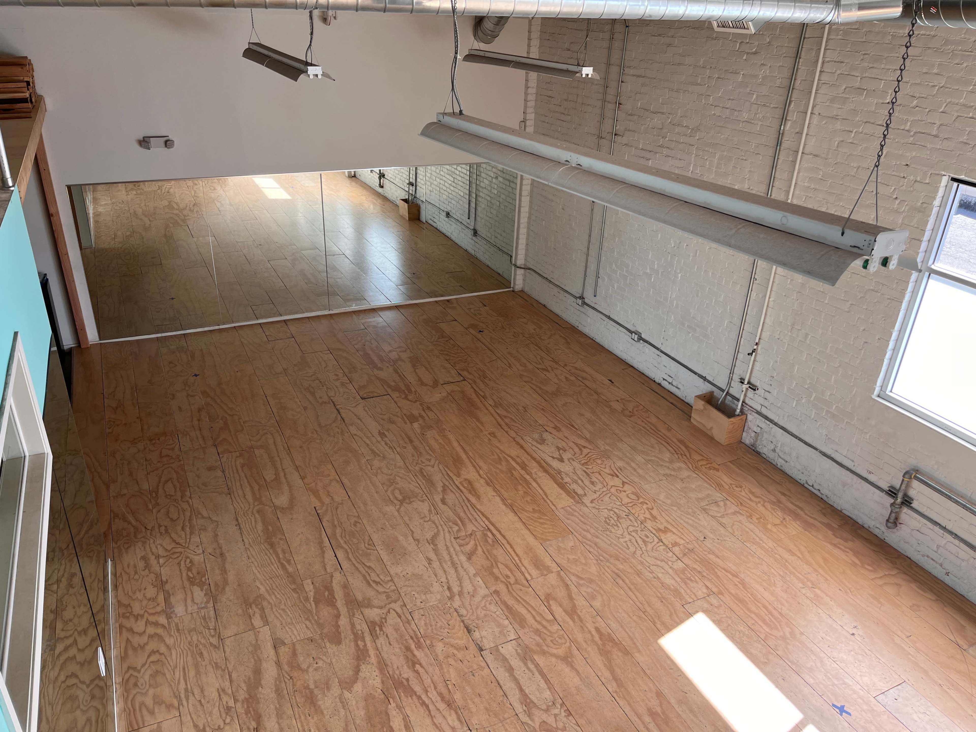A spacious interior with hardwood flooring, large windows, and a mirrored wall reflecting the room's layout.