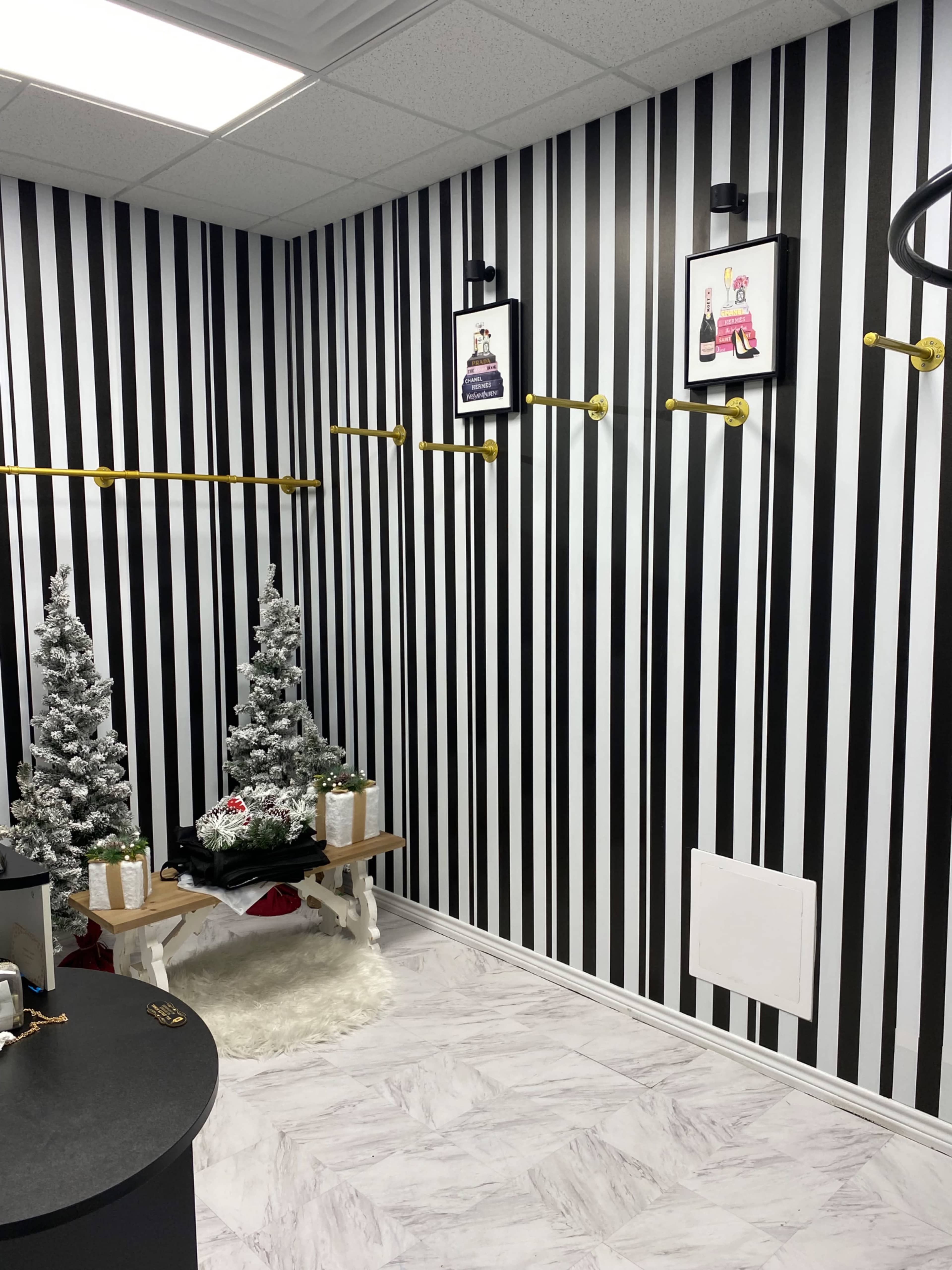 The image shows a shop interior with black and white striped walls, two small artificial Christmas trees, and framed pictures mounted on the wall.