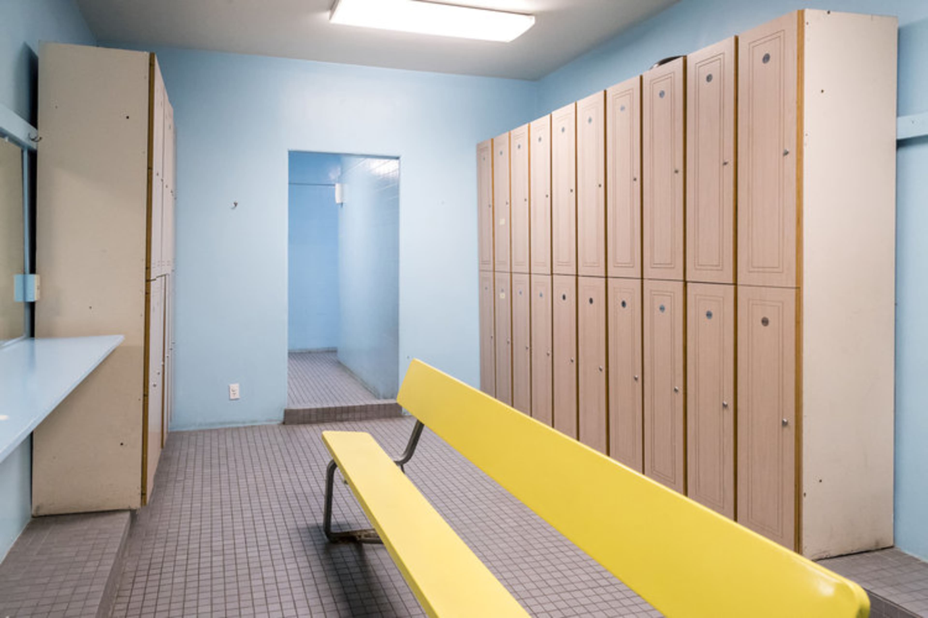 A locker room with a yellow bench and beige lockers against light blue walls.