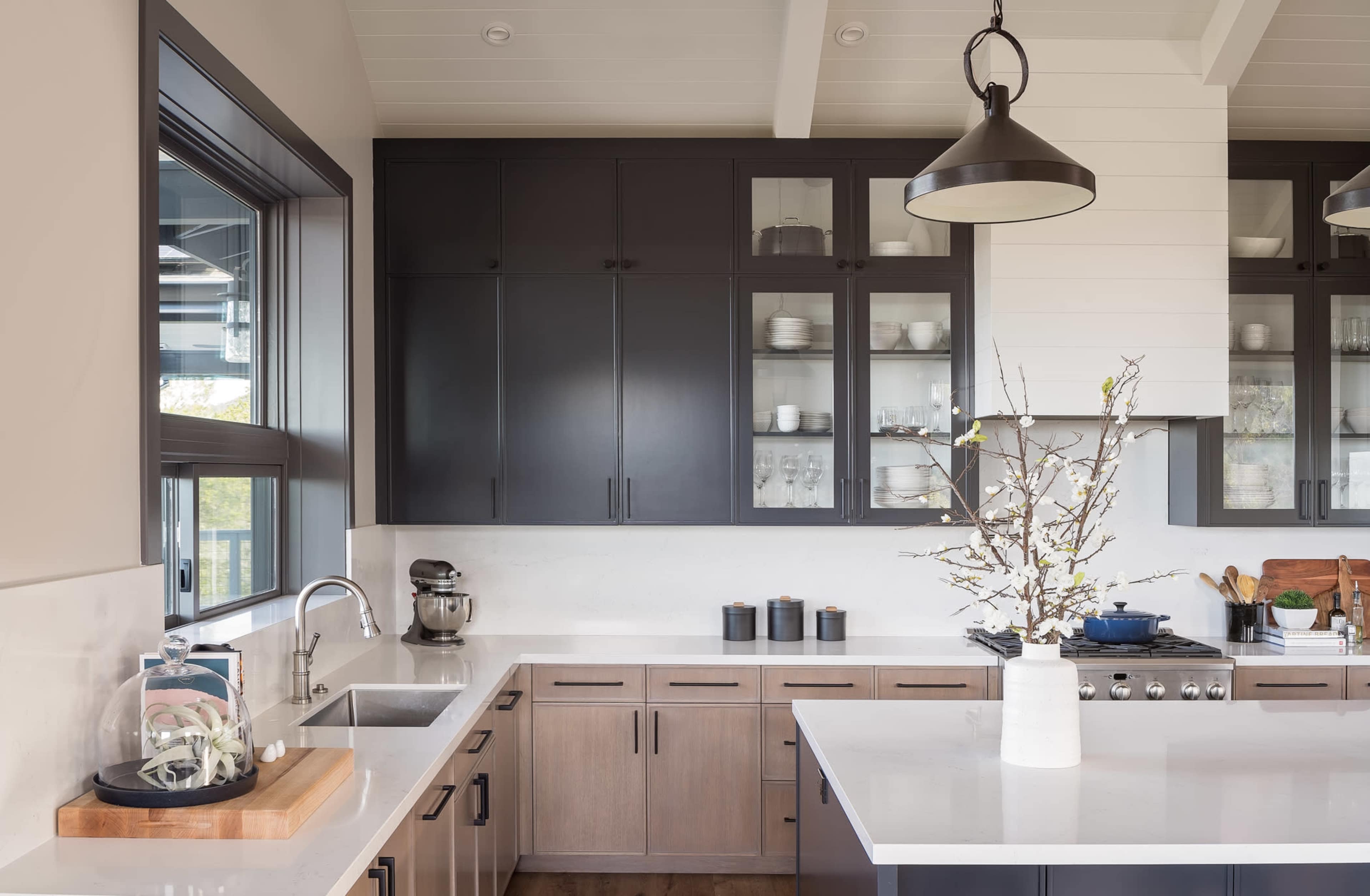 A modern kitchen with dark cabinets, a white countertop, and a central island featuring a decorative branch centerpiece.