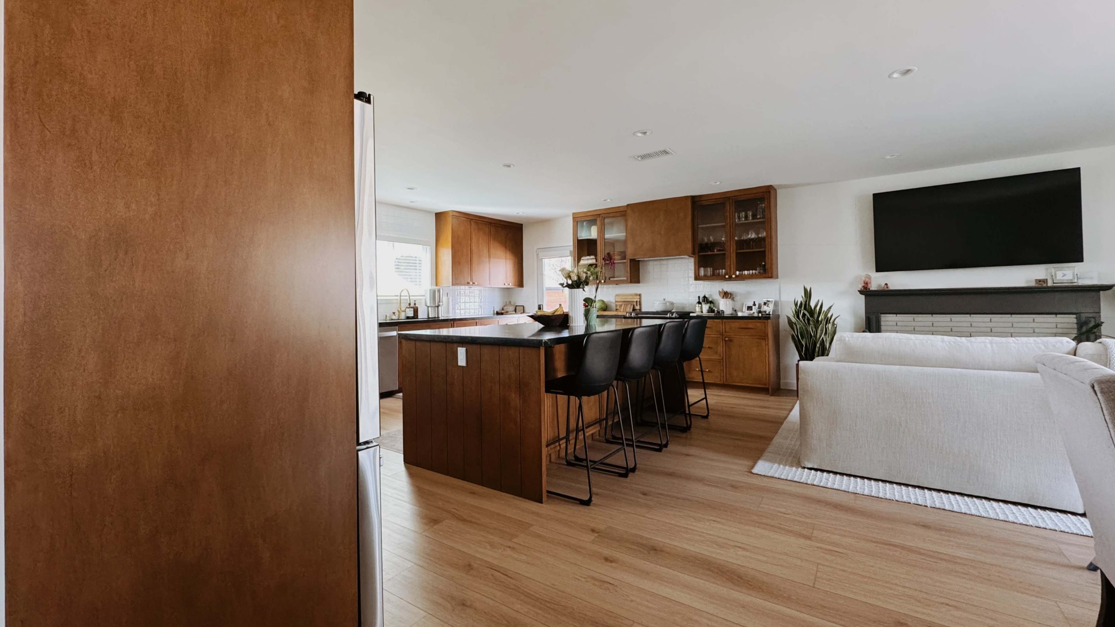 A spacious kitchen features wooden cabinets, a large island with bar stools, and a cozy seating area with a television.