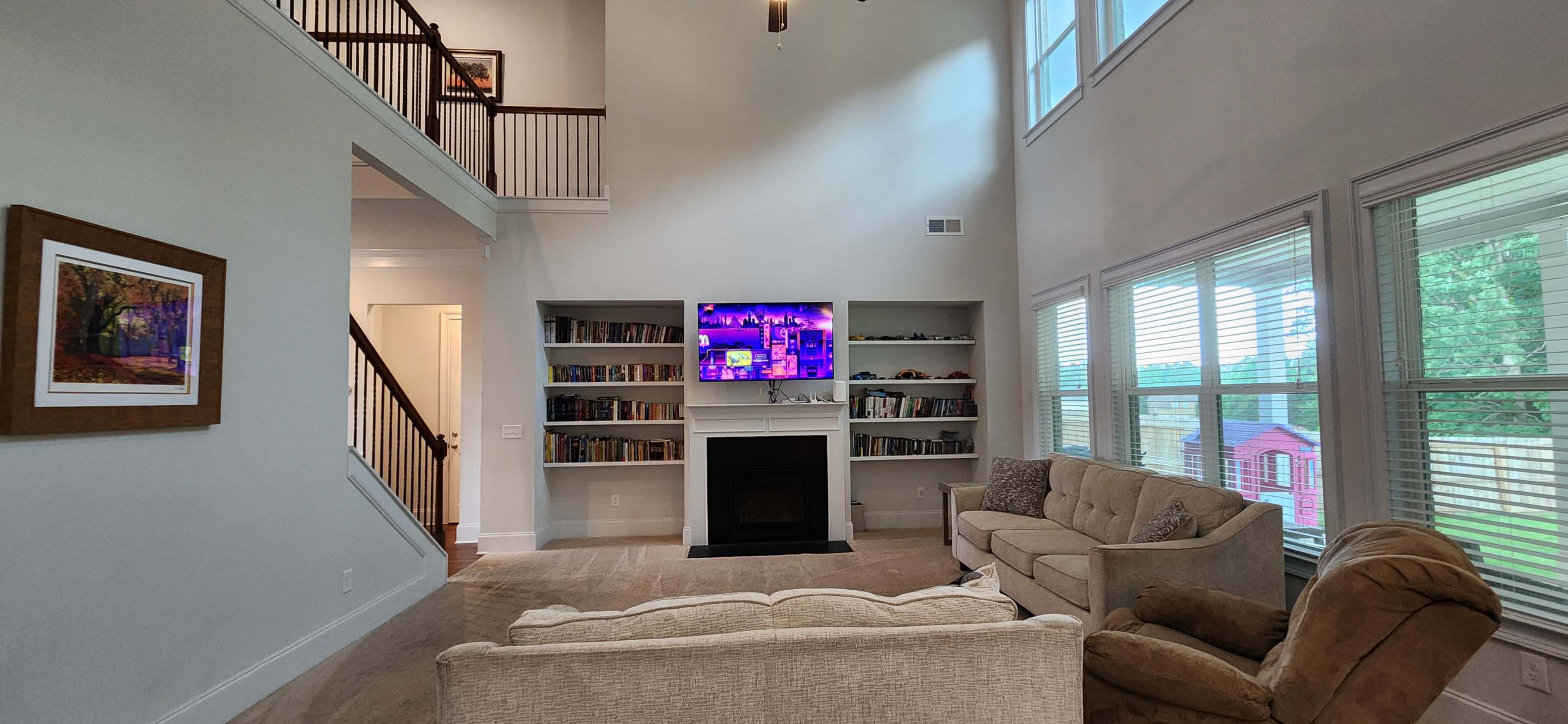 The living room features high ceilings, a fireplace, a large TV mounted on the wall, and bookshelves filled with books.