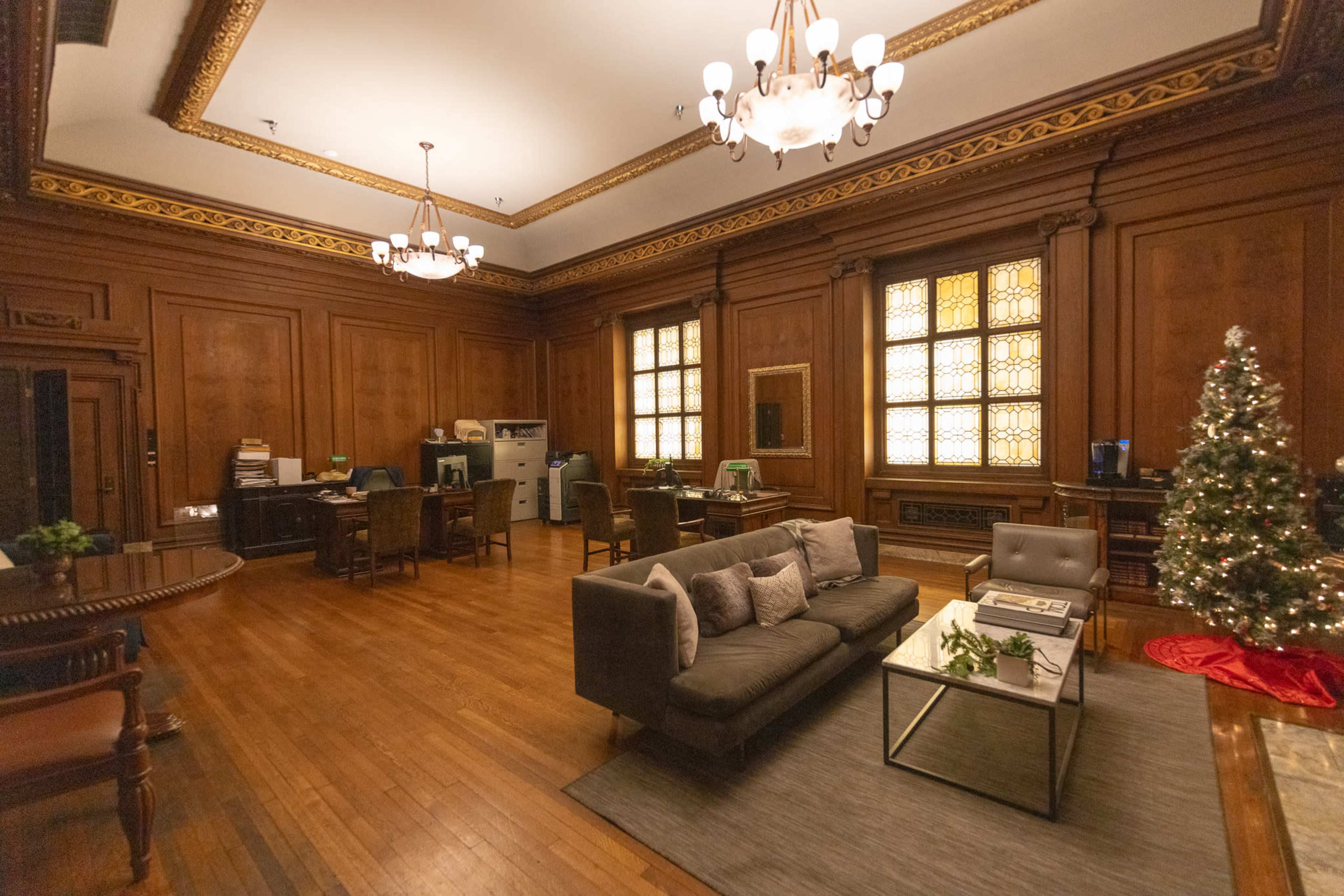 The image shows an elegantly furnished room featuring wooden paneling, a Christmas tree, and several workstations.