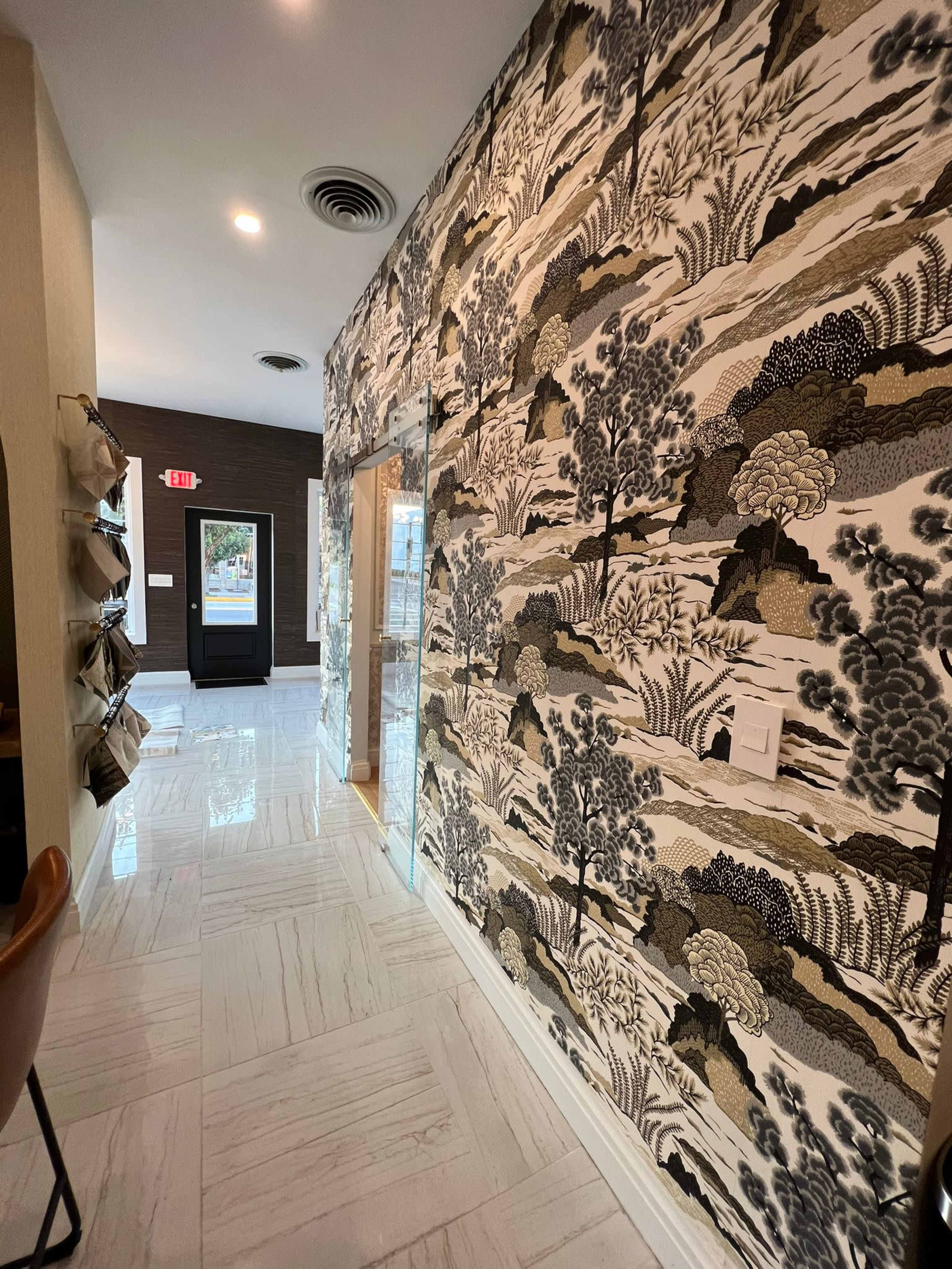 A hallway with a patterned wallpaper featuring trees and foliage, and glossy white tile flooring.