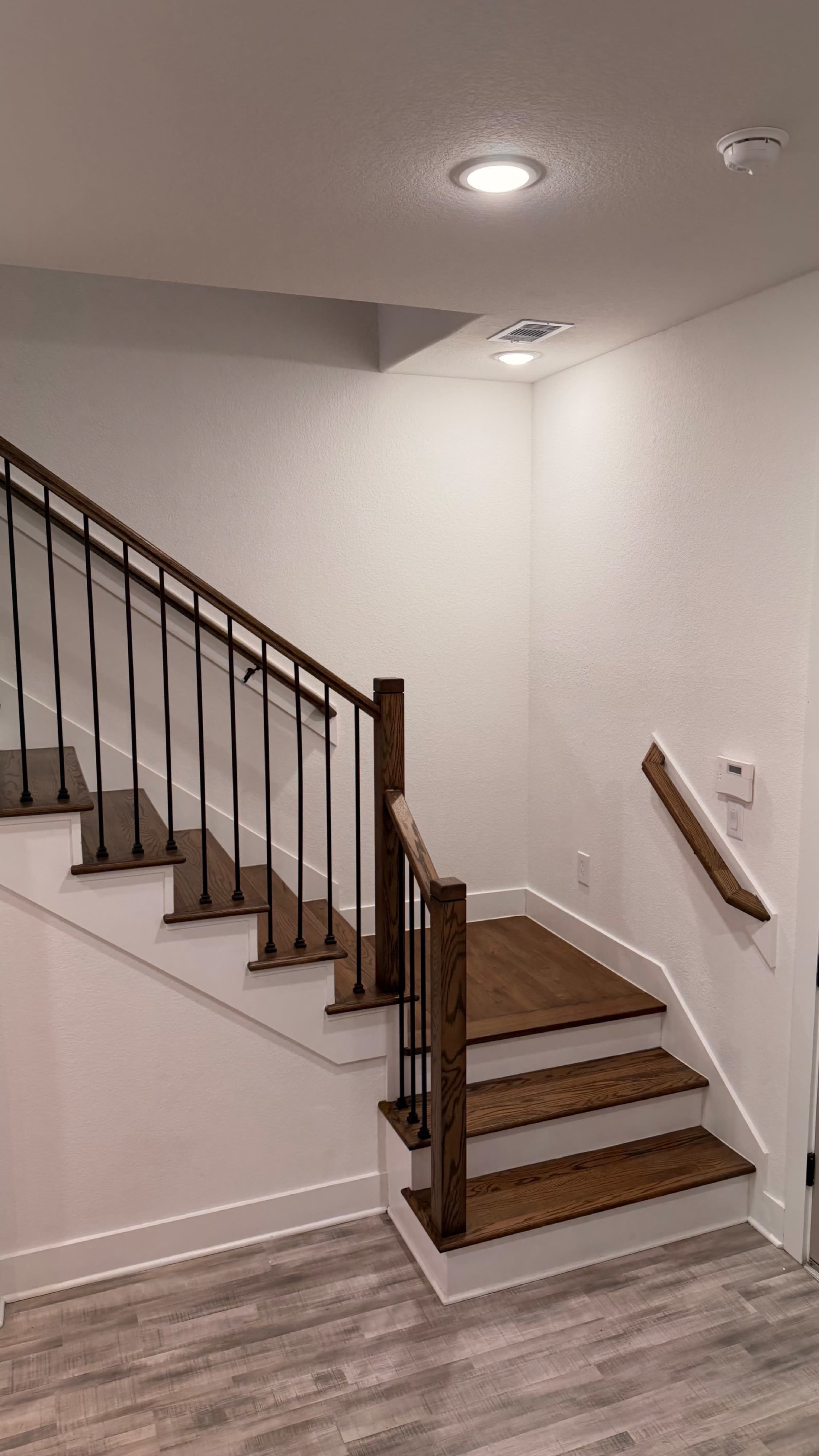 The image shows a staircase with wooden steps and a black metal railing, leading to an upper level in a well-lit interior space.