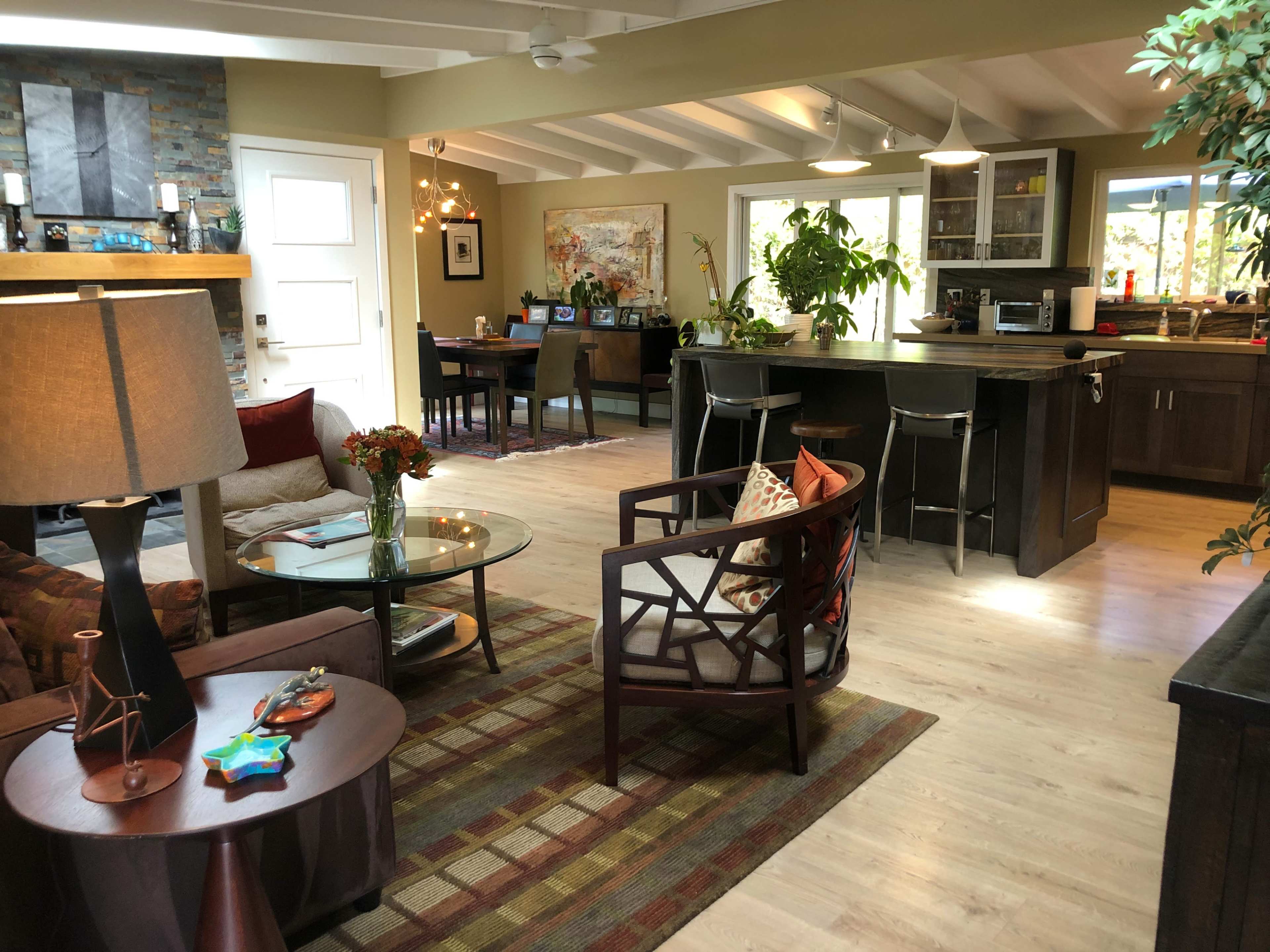 A spacious living area with a mix of modern and traditional furnishings, featuring a coffee table, chairs, and a dining area with computers and plants.