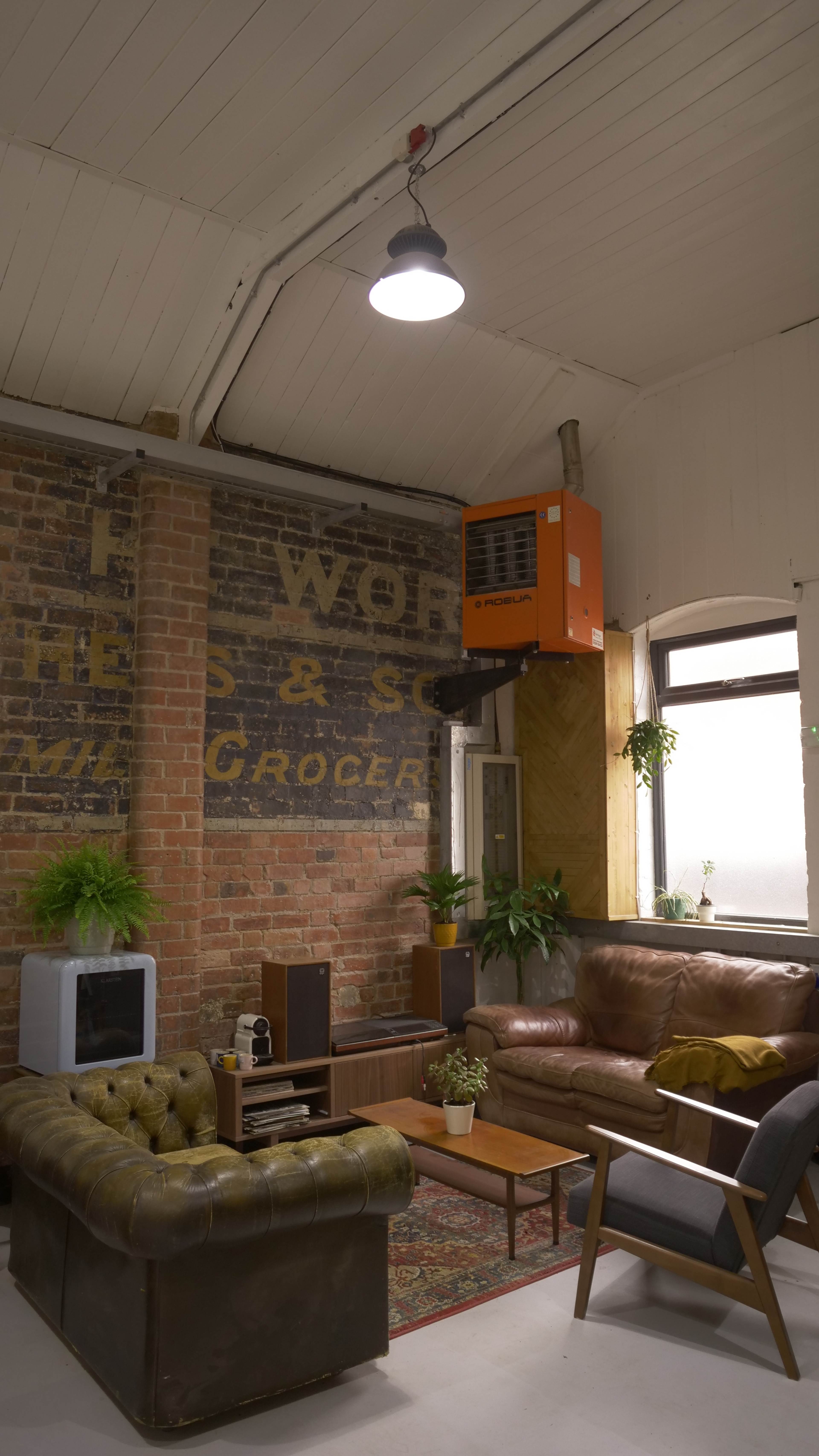 A cozy living room with a brown leather sofa, a green upholstered chair, a wooden coffee table, and exposed brick walls featuring vintage signage.
