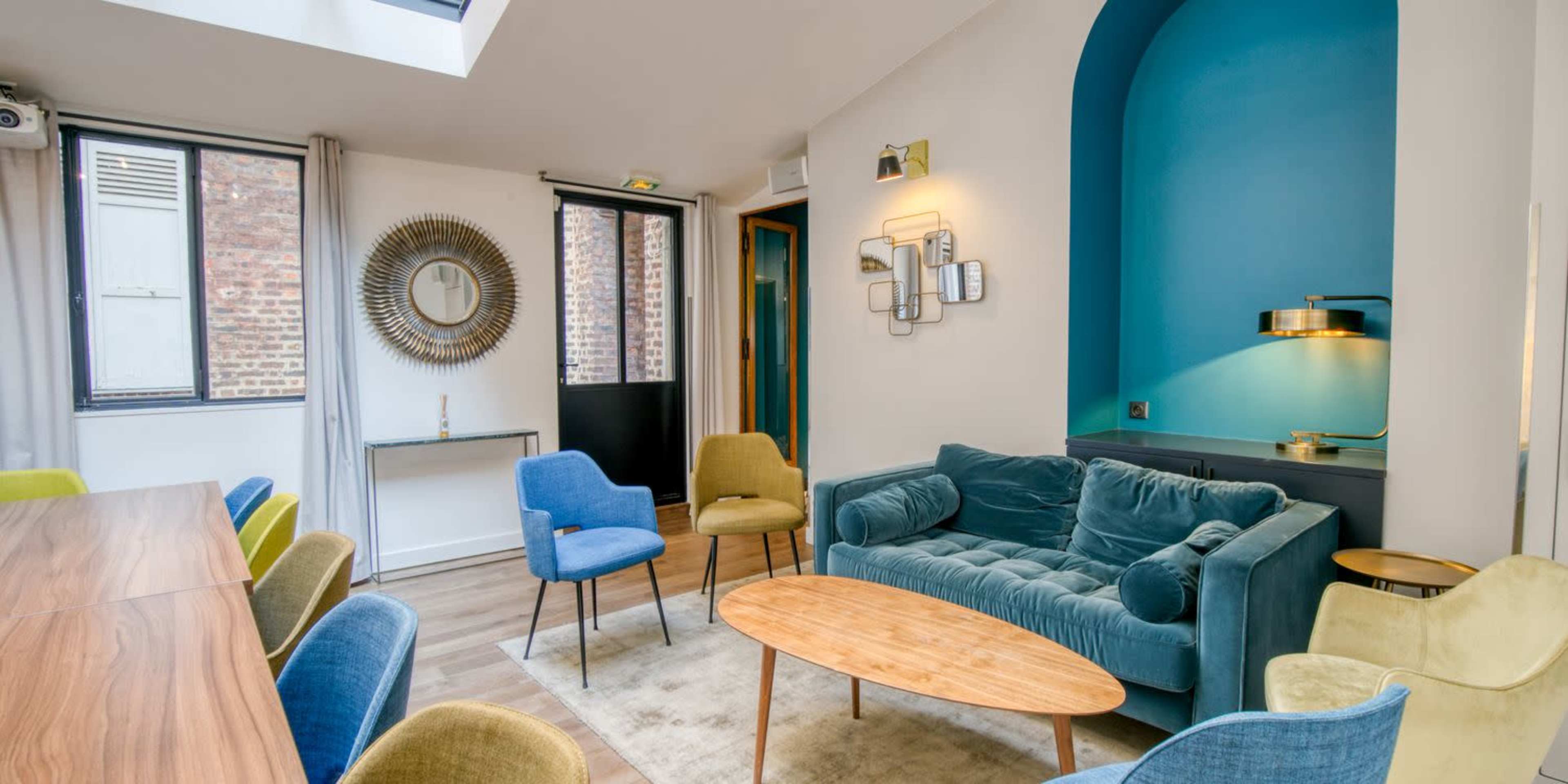 A modern living space with a blue accent wall, a group of colorful chairs, a wooden table, and a plush sofa.
