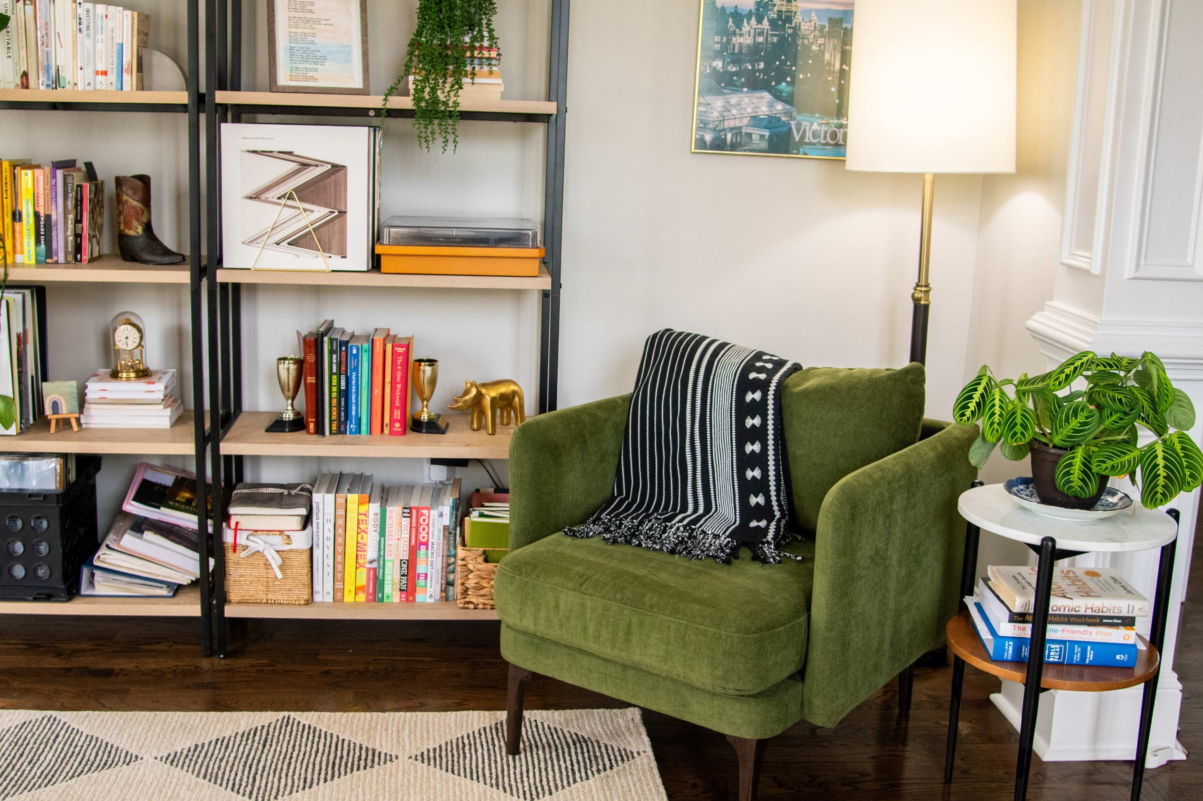The image shows a cozy reading nook with a green armchair, a small side table, and a bookshelf filled with various books and decorative items.