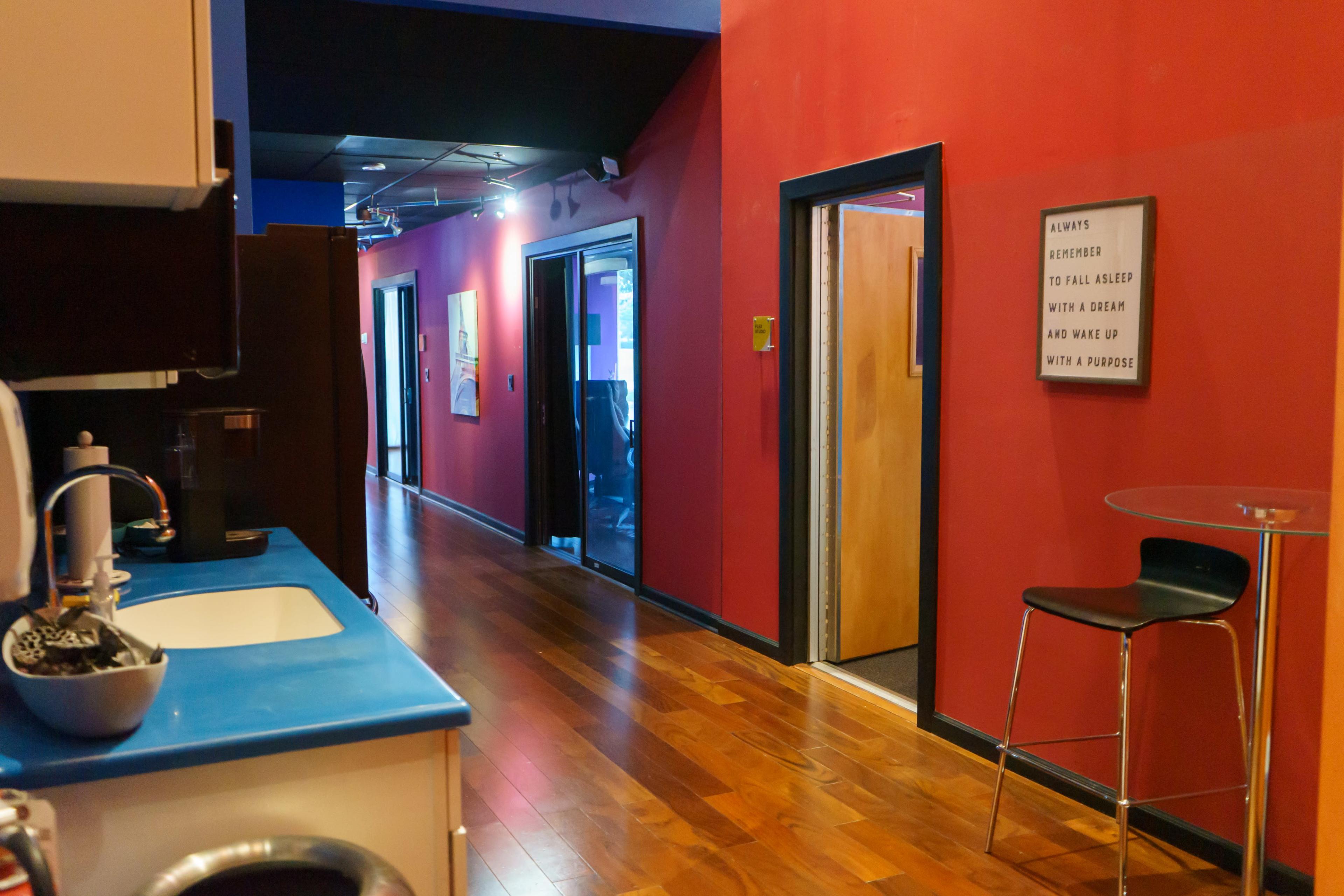 A modern hallway with red walls features doors leading to various offices, while a kitchen area is visible on the left side.