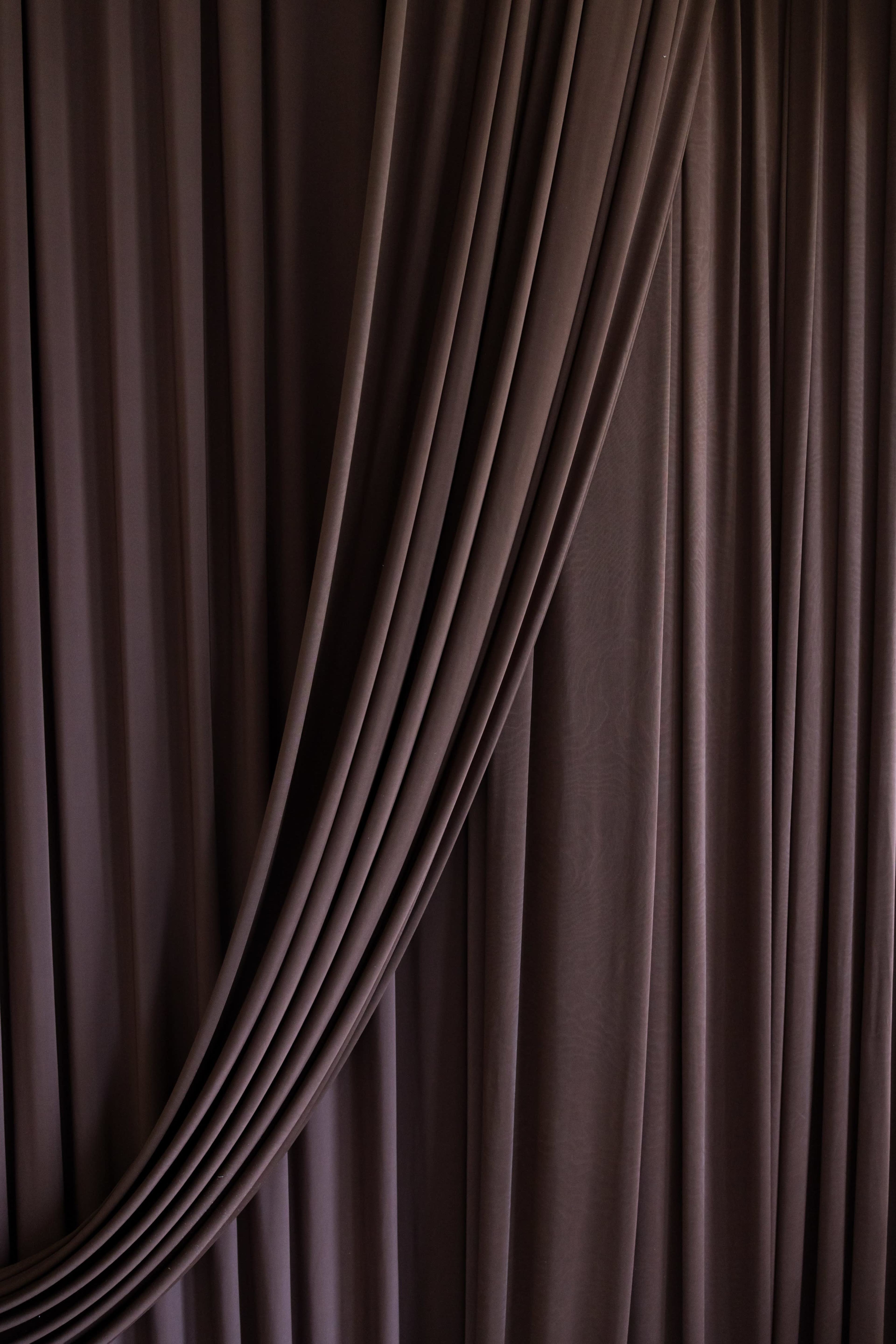 The image shows a set of dark, draped curtains with soft folds and a smooth texture.
