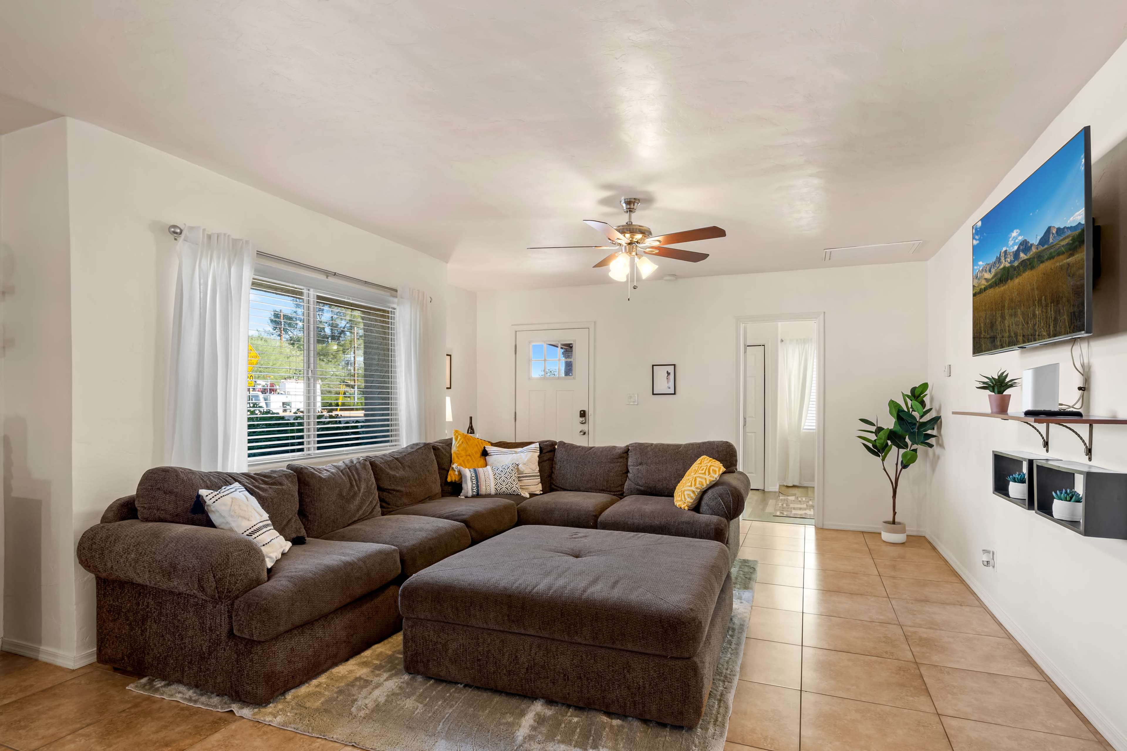 The living room features a large brown sectional sofa, a ceiling fan, and a TV mounted on the wall.