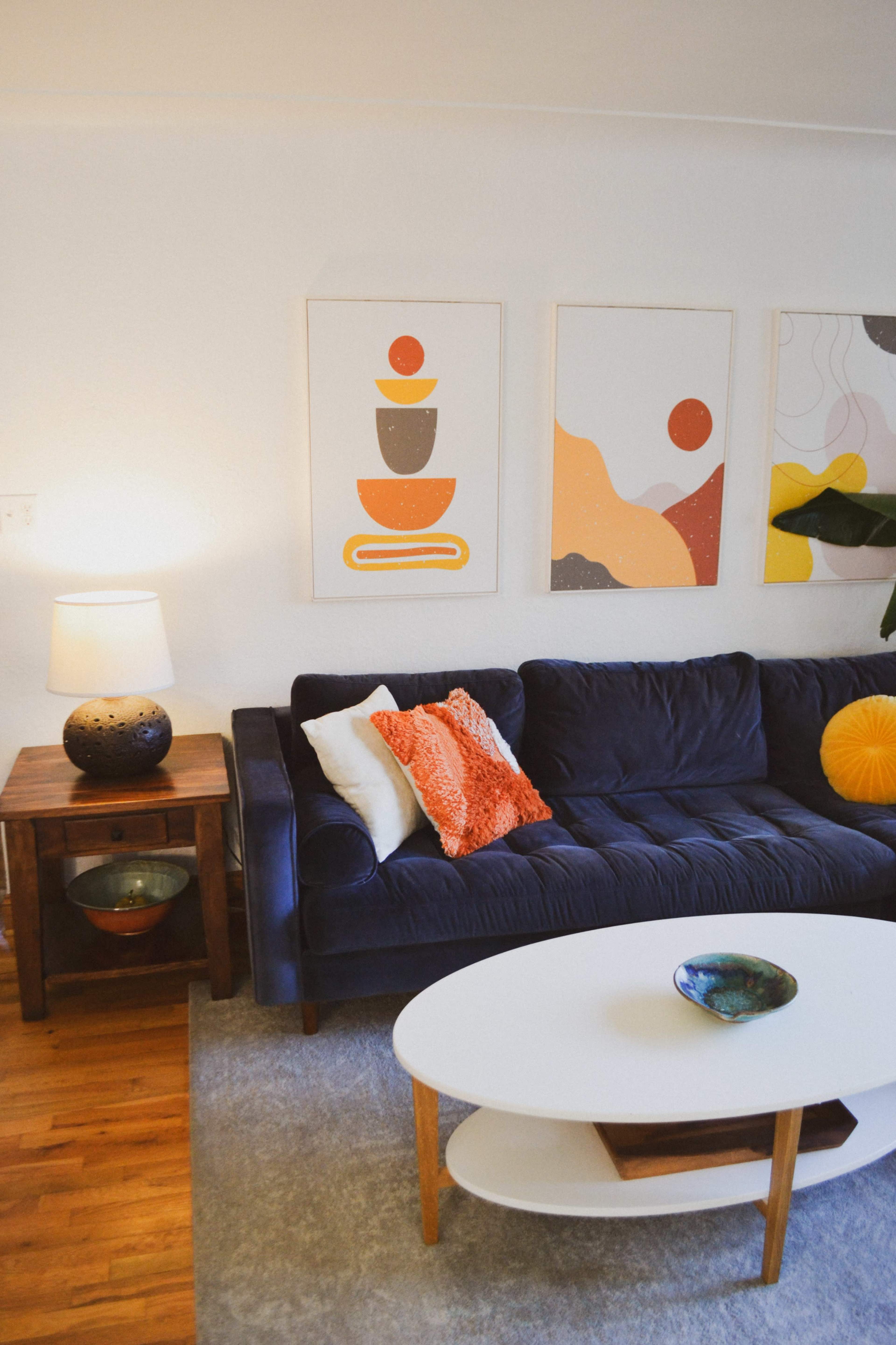 The image shows a living room featuring a dark blue sofa, a round white coffee table, and three framed wall art pieces above the sofa.