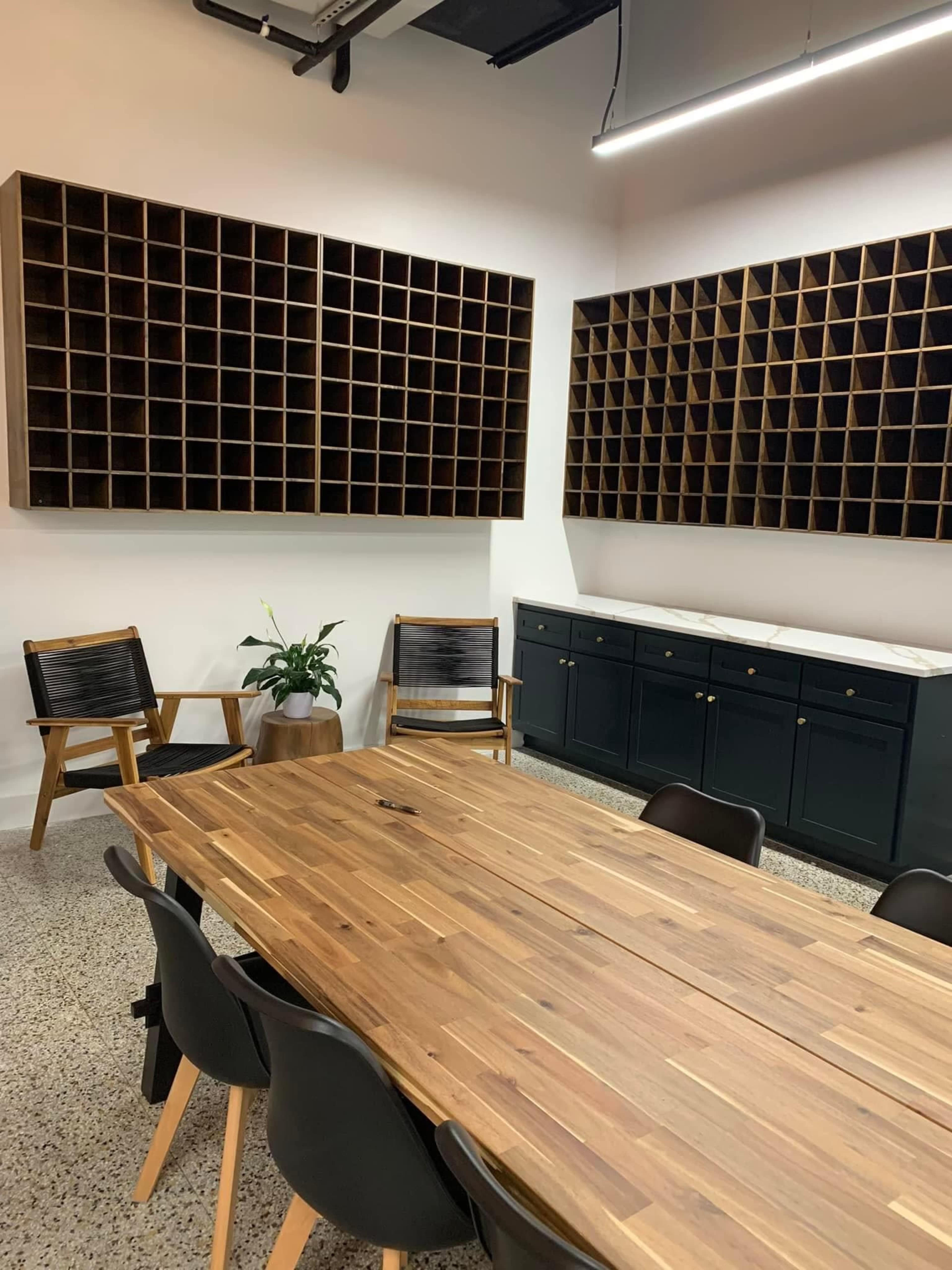 A conference room features a large wooden table surrounded by chairs, with wooden cubby shelves and a cabinet along the walls.