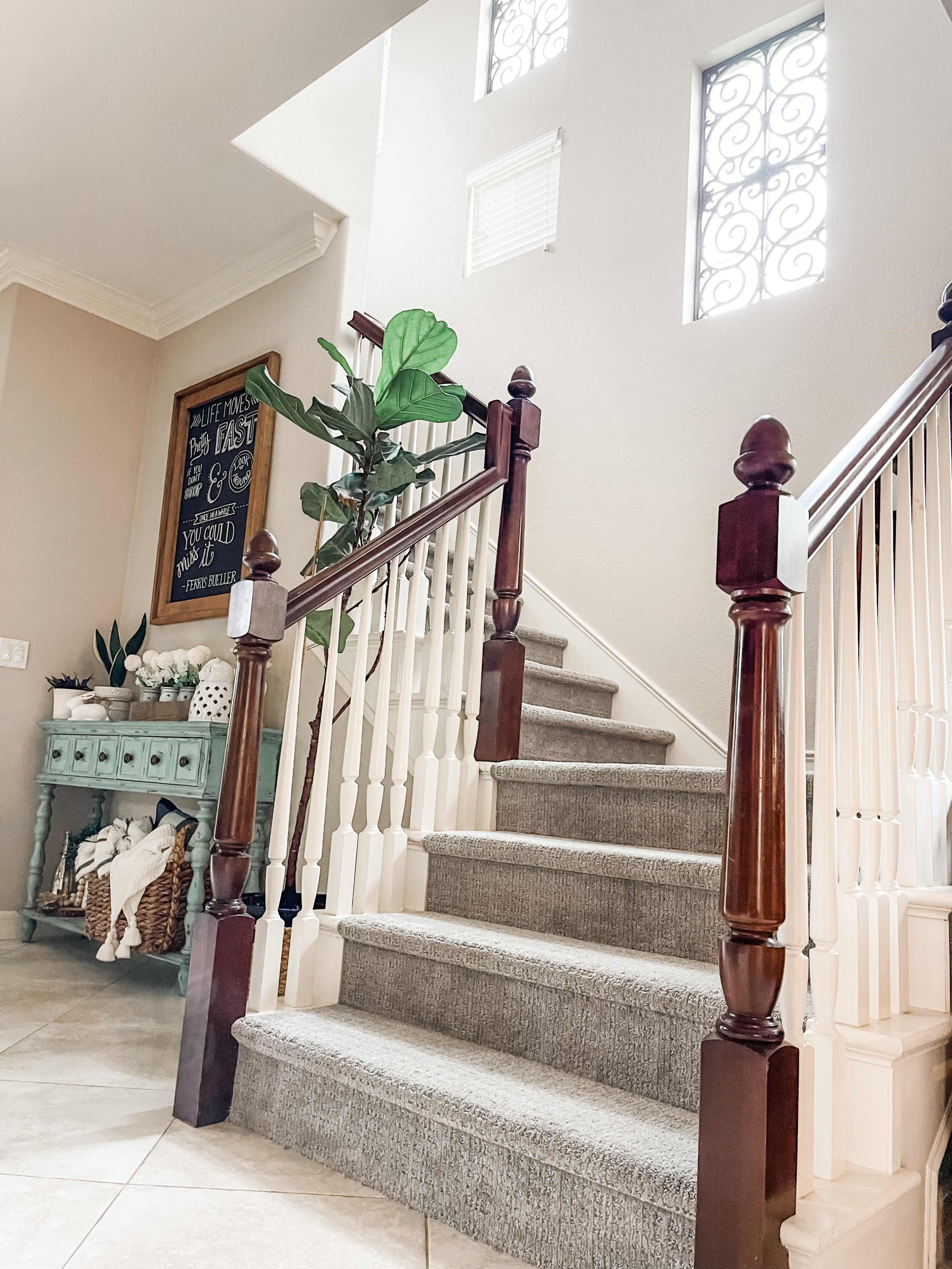 A staircase with wooden railings, leading to a light-filled upper level, accompanied by decorative elements like plants and a console table.