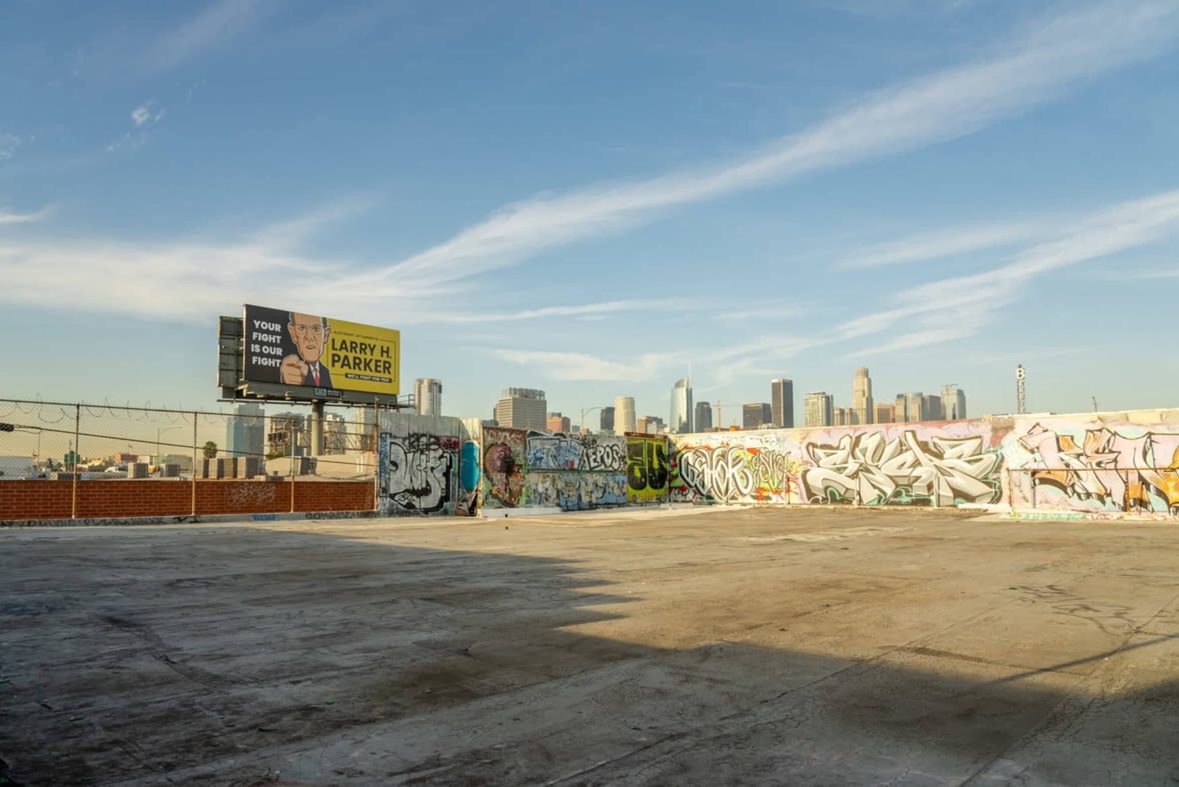 The image shows a rooftop space covered in colorful graffiti, with a distant skyline of tall buildings against a clear blue sky.