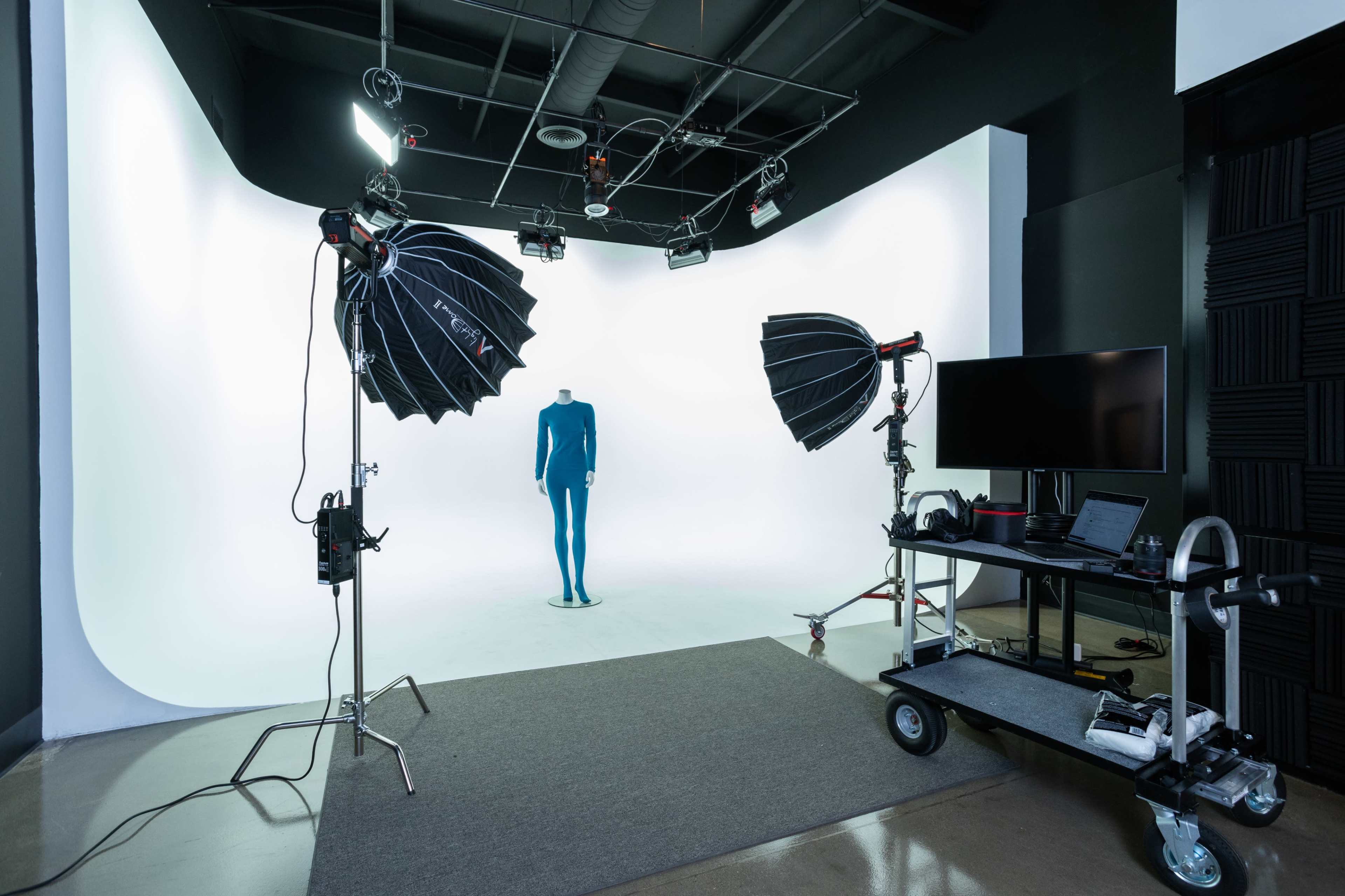 A photography studio setup with two large light sources aimed at a blue mannequin positioned on a backdrop.