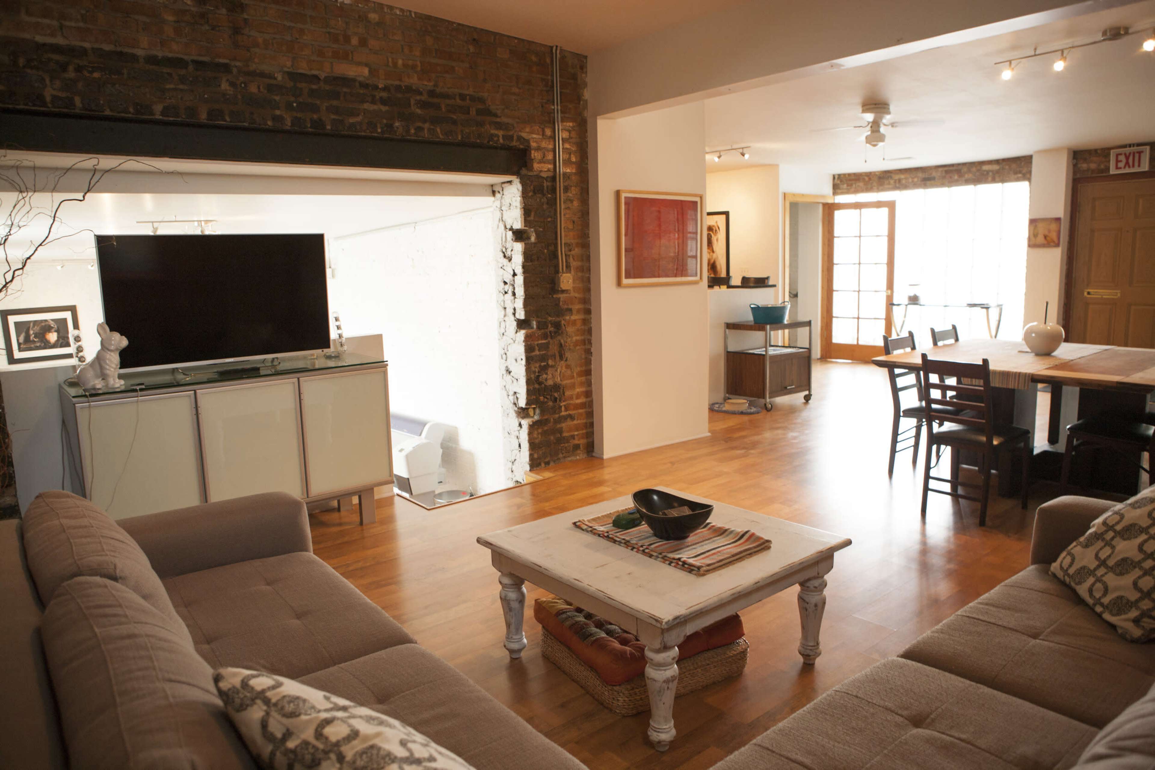 A modern living room with a television on a wall unit, a coffee table in the center, and an open layout leading to a dining area.