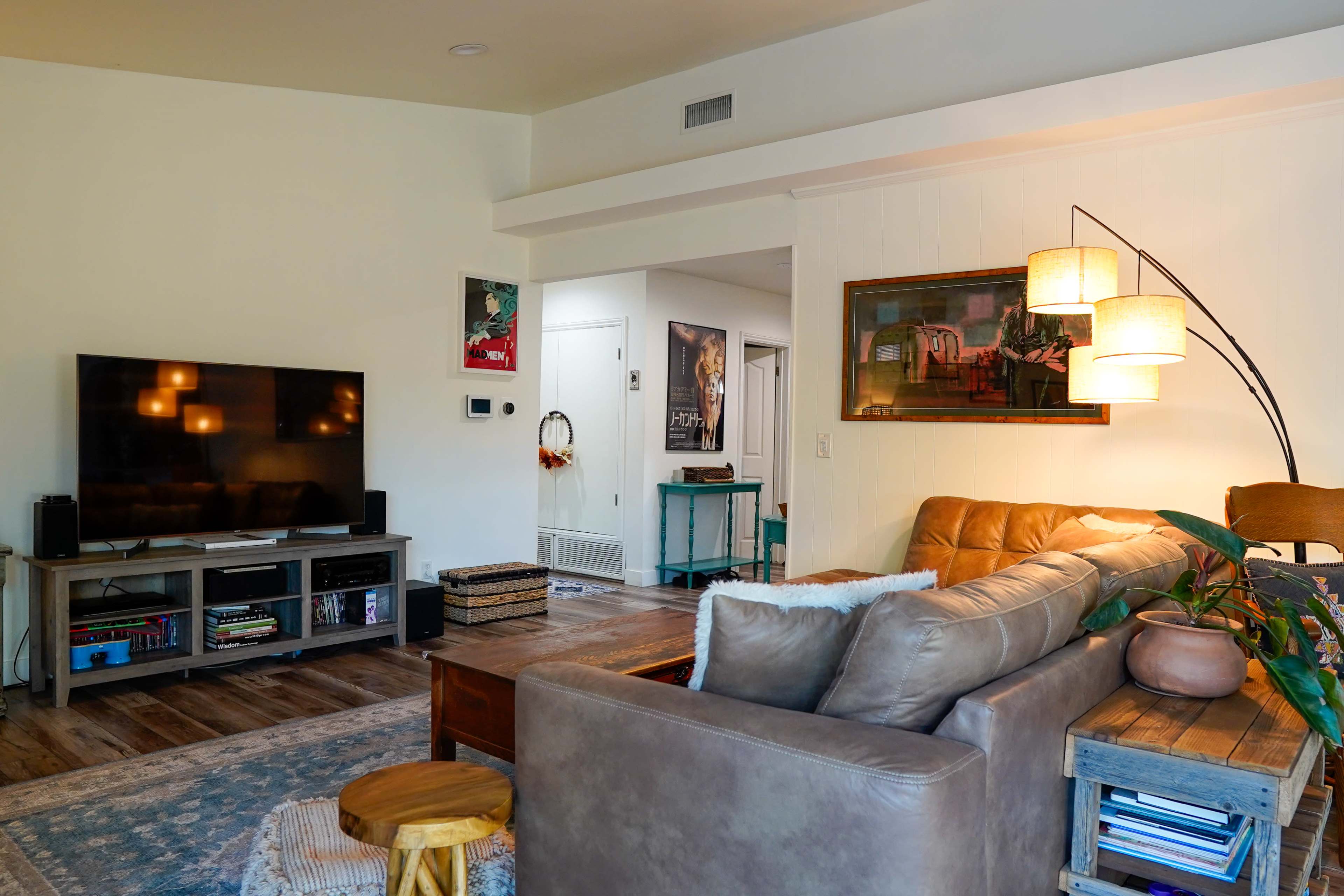 The image shows a modern living room with a sectional sofa, a television stand, a coffee table, and decorative elements throughout the space.