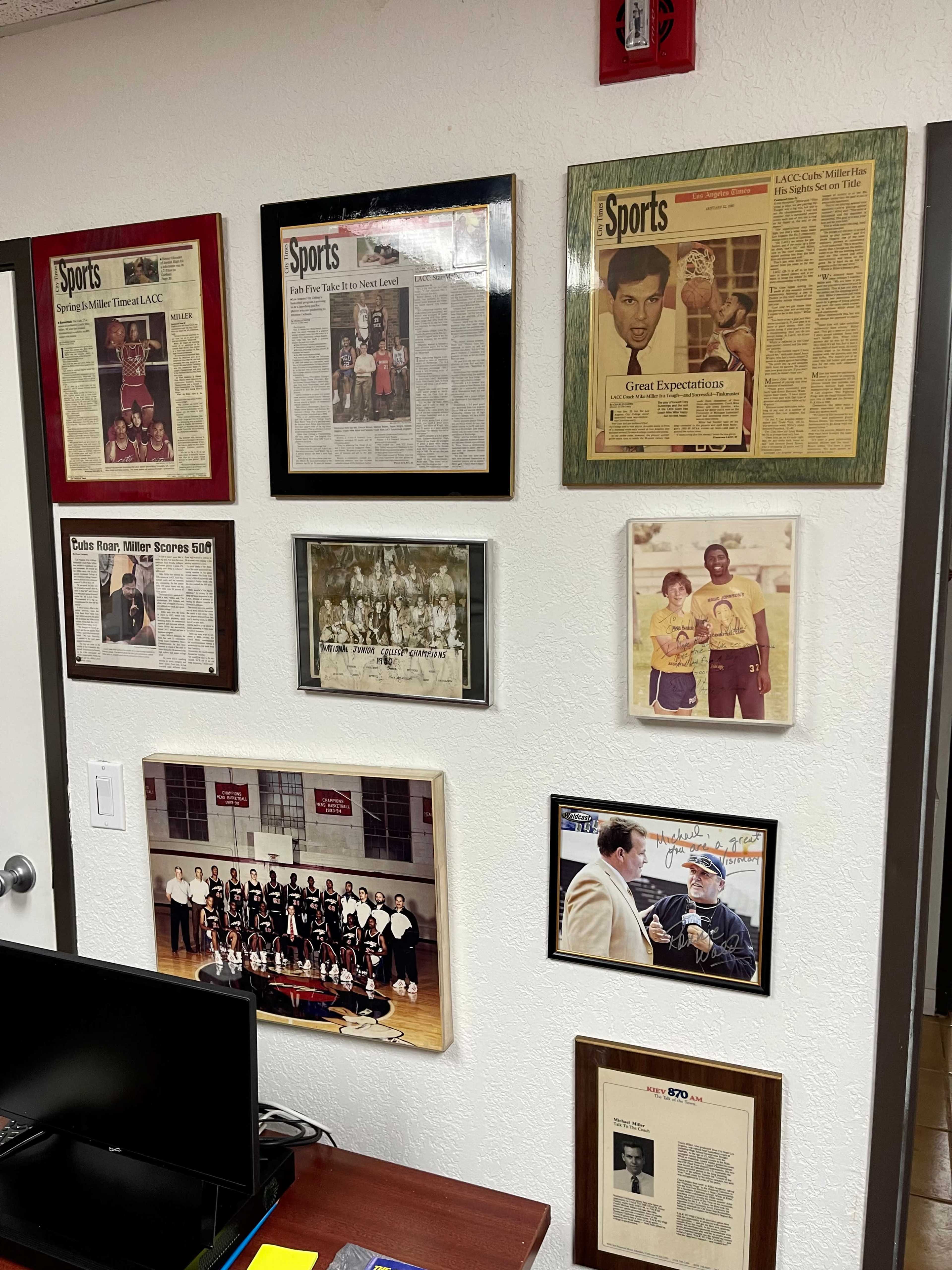 The wall features a collection of framed newspaper articles, photographs, and memorabilia dedicated to sports achievements and events.
