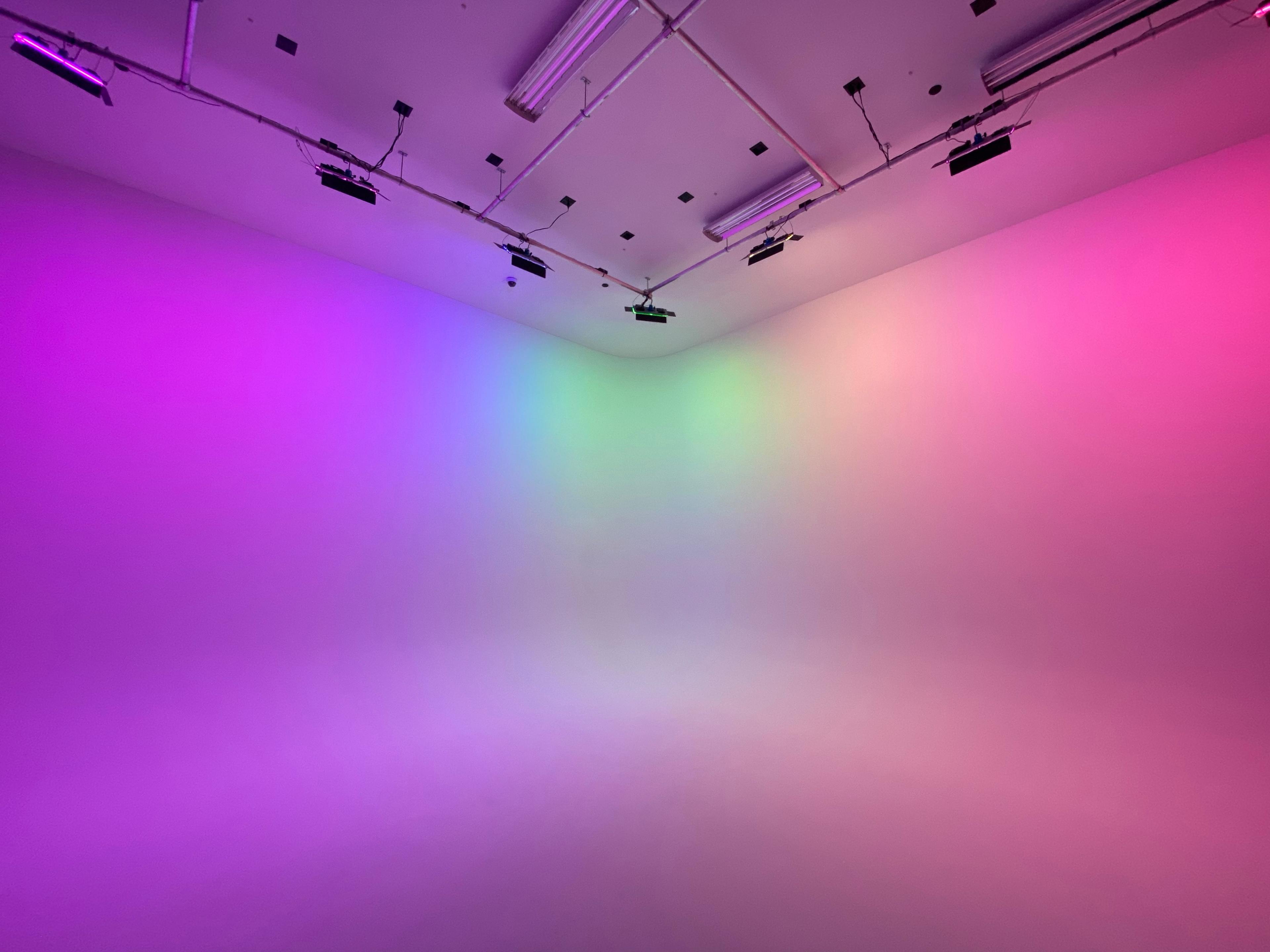 A studio space features walls illuminated with gradient purple and green lighting.