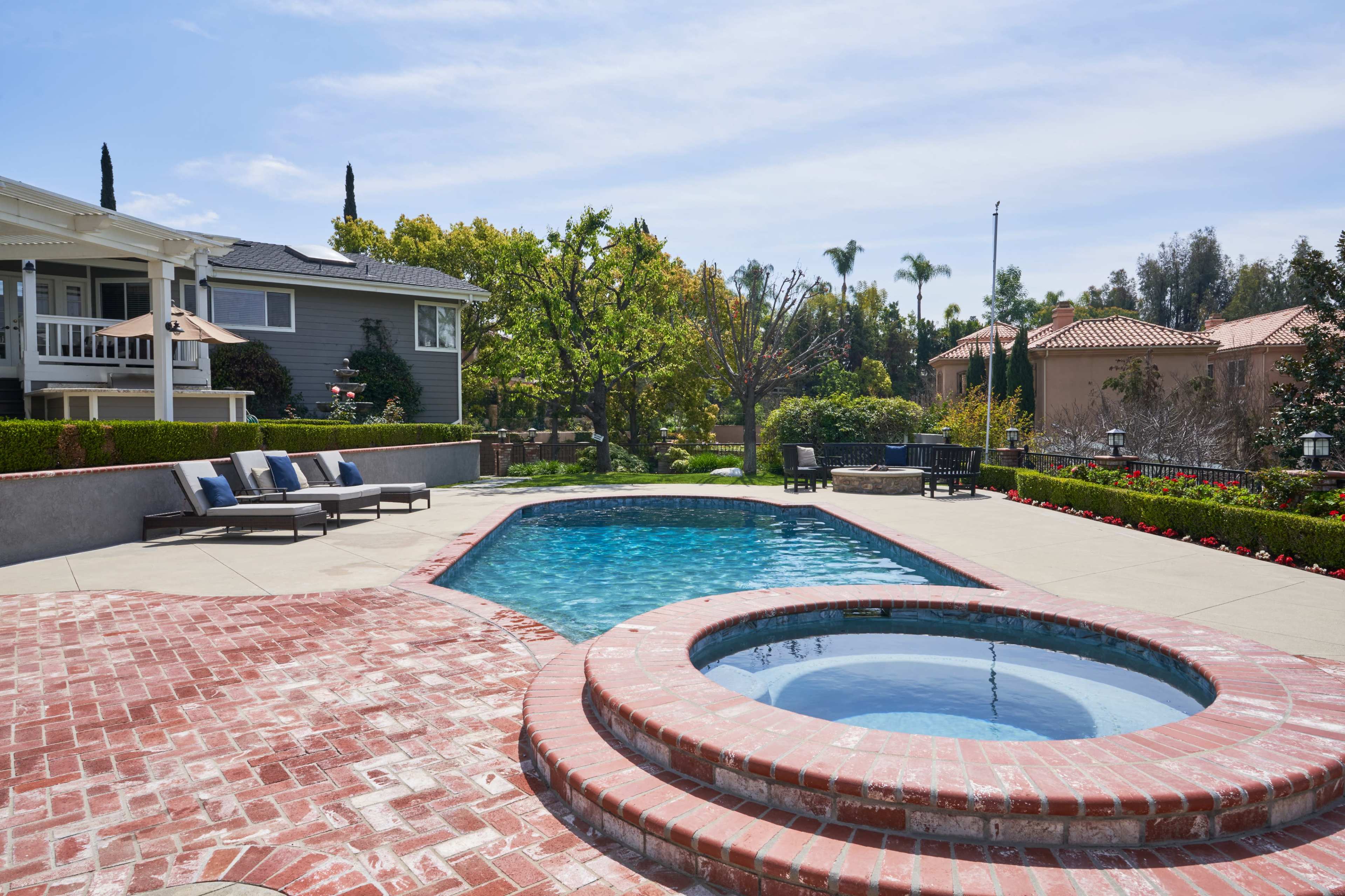 A backyard with a swimming pool and a spa, surrounded by landscaped greenery and residential buildings.