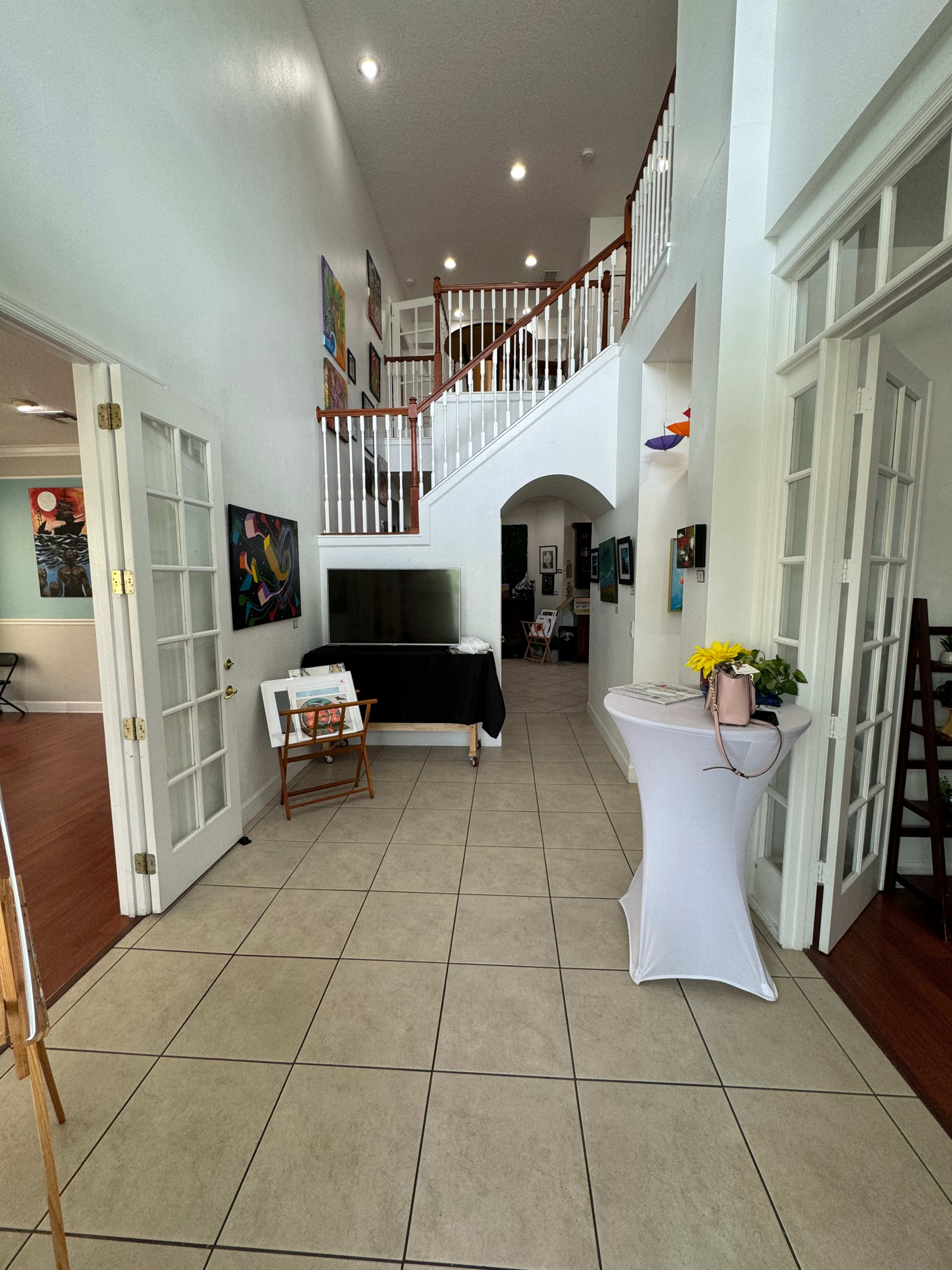 A bright hallway with a staircase, featuring tiled flooring, a reception table, and several pieces of artwork on the walls.