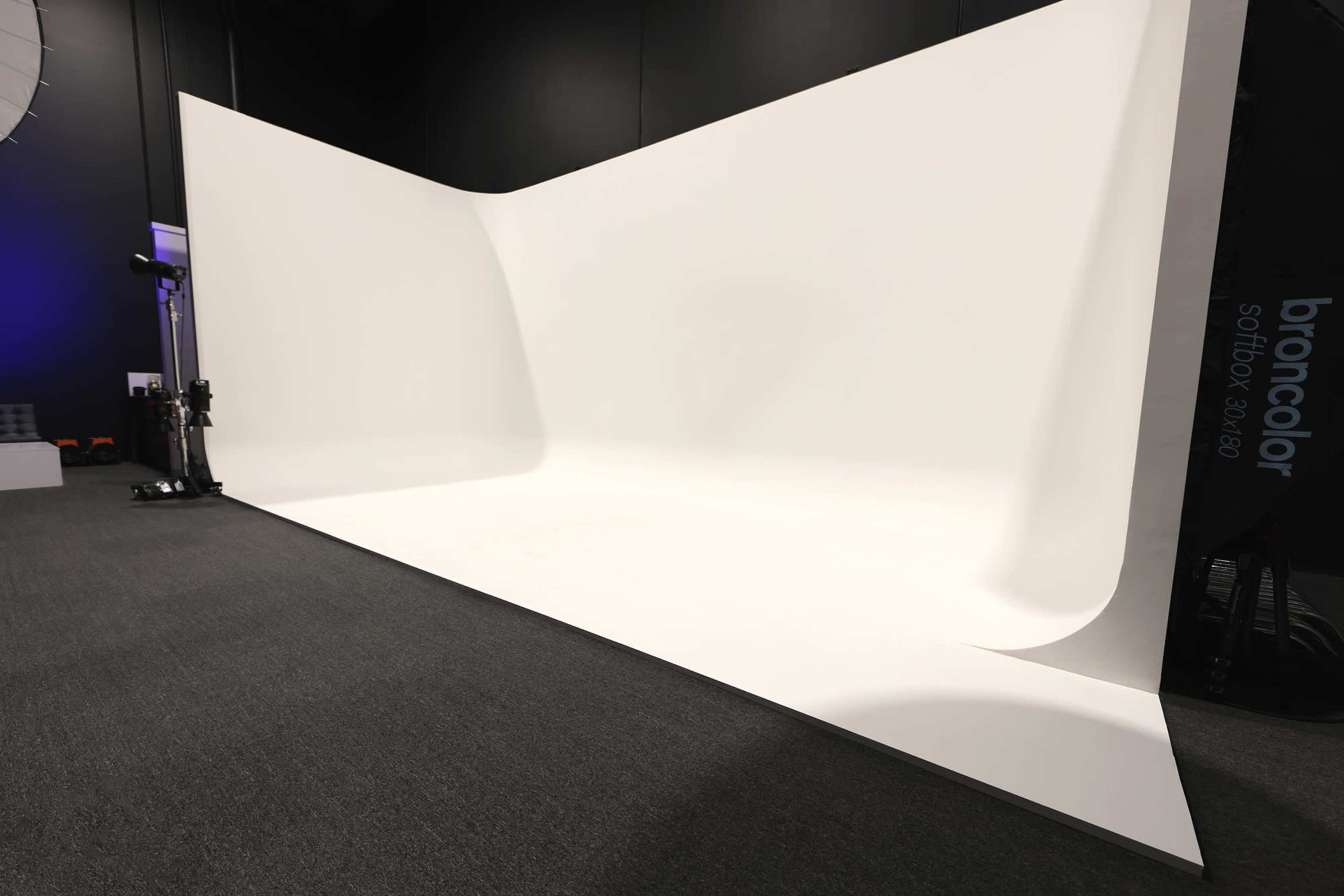 A spacious photography studio with a seamless white backdrop and dark gray carpet.