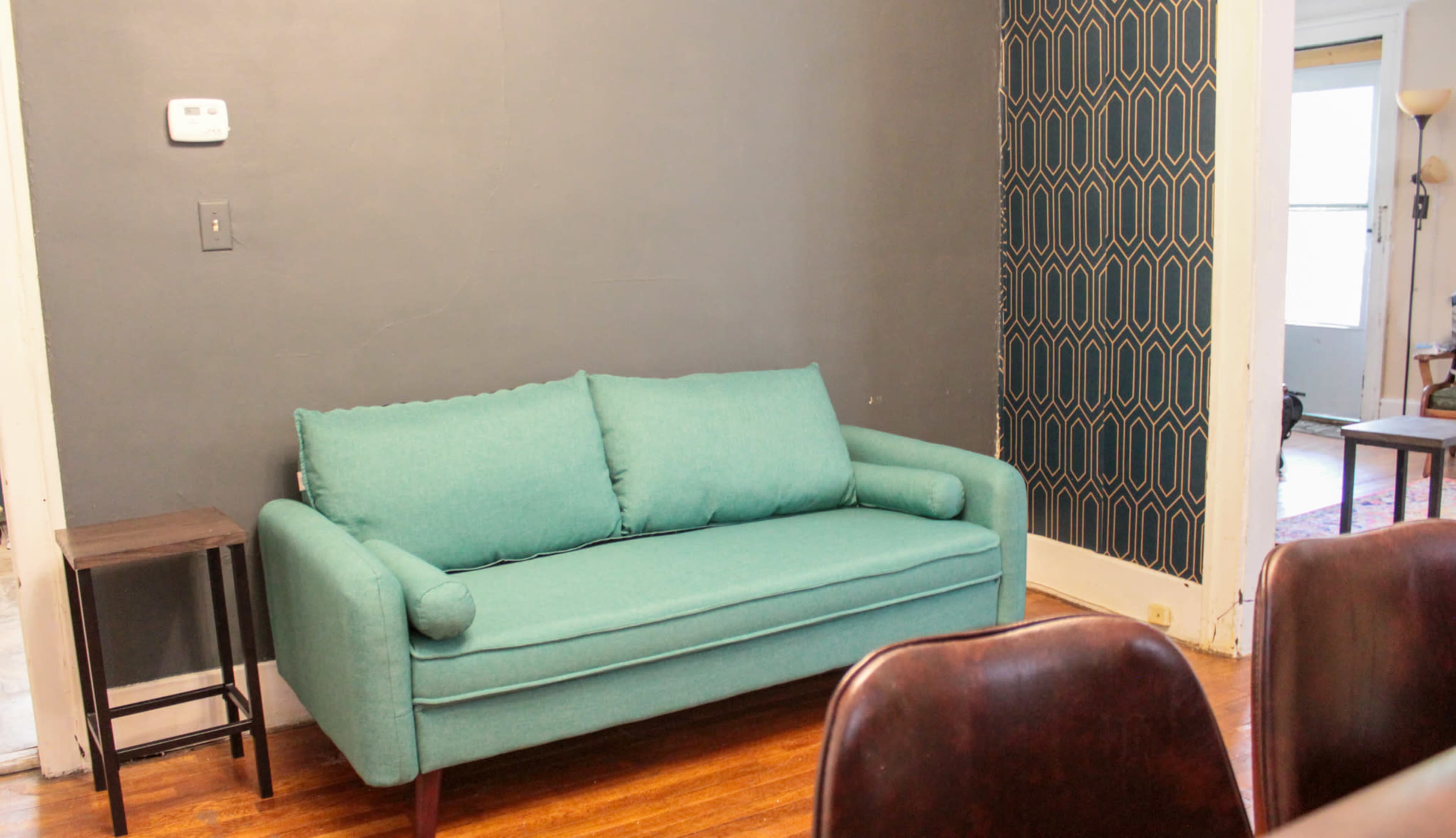 A light teal sofa against a gray wall, with a small black side table nearby and a patterned wallpaper on the right.
