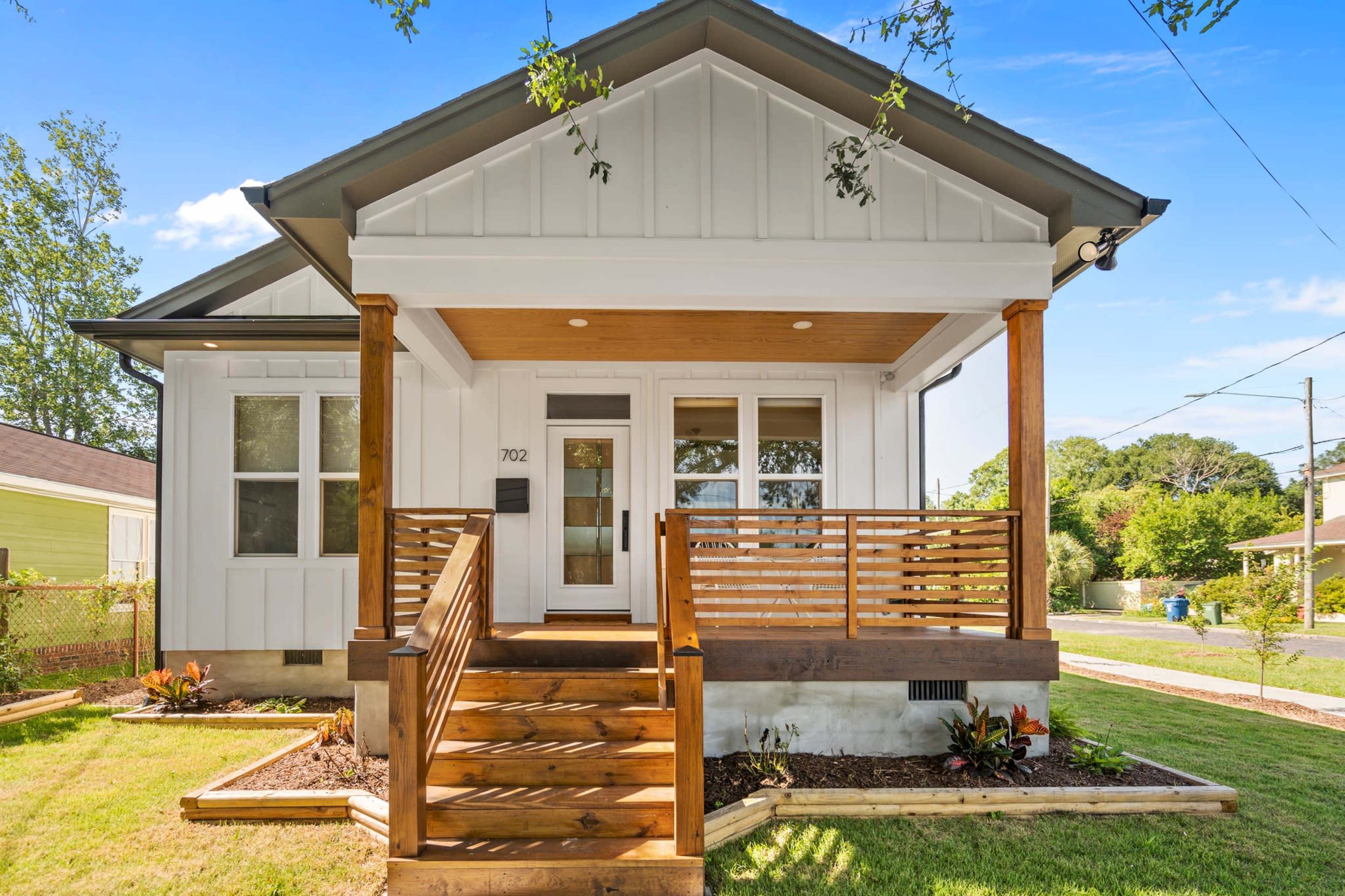 A modern white house with a wooden porch and steps features a landscaped front yard.