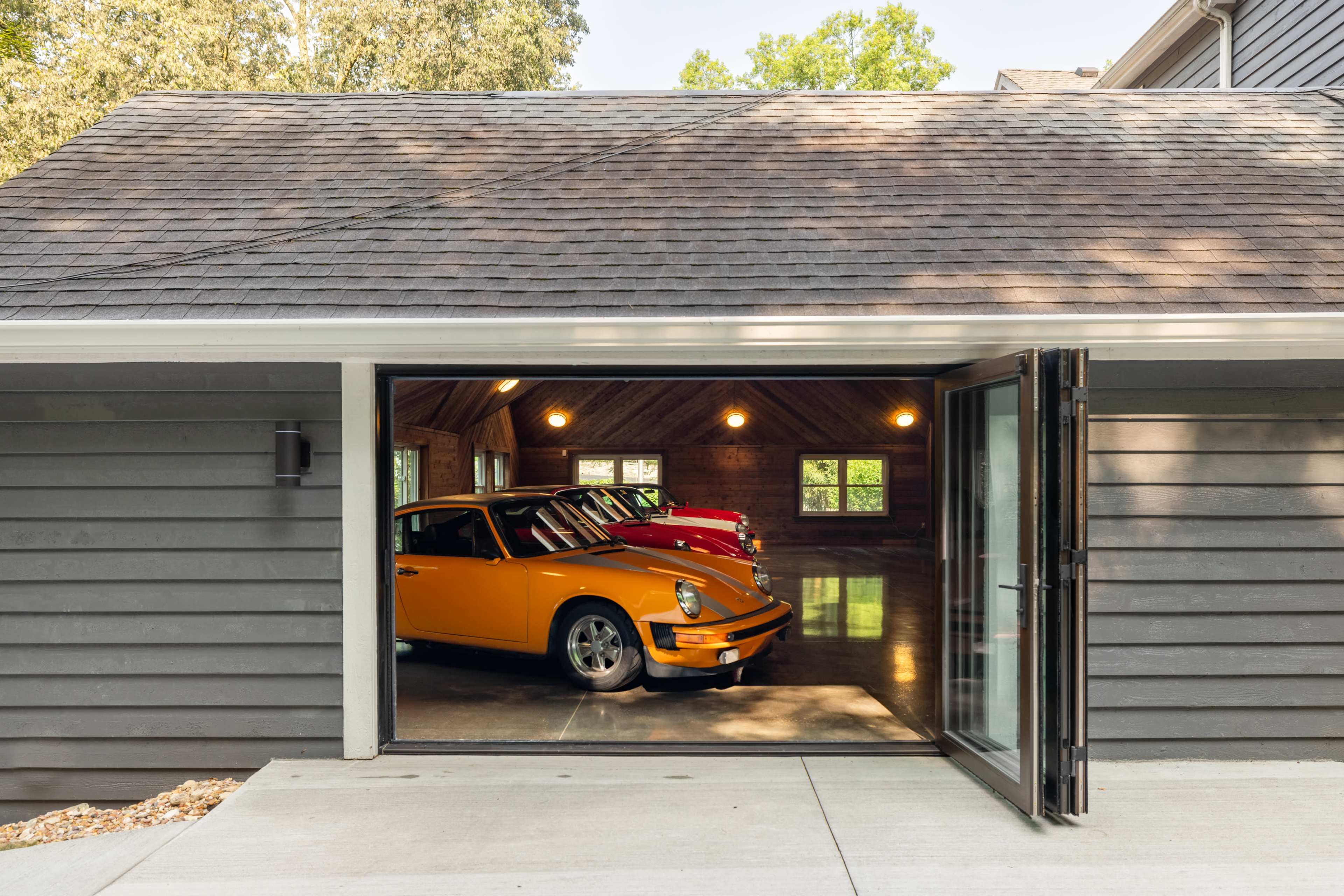 A partially open garage with two classic cars, one orange and one red, parked inside against a wooden-paneled wall.