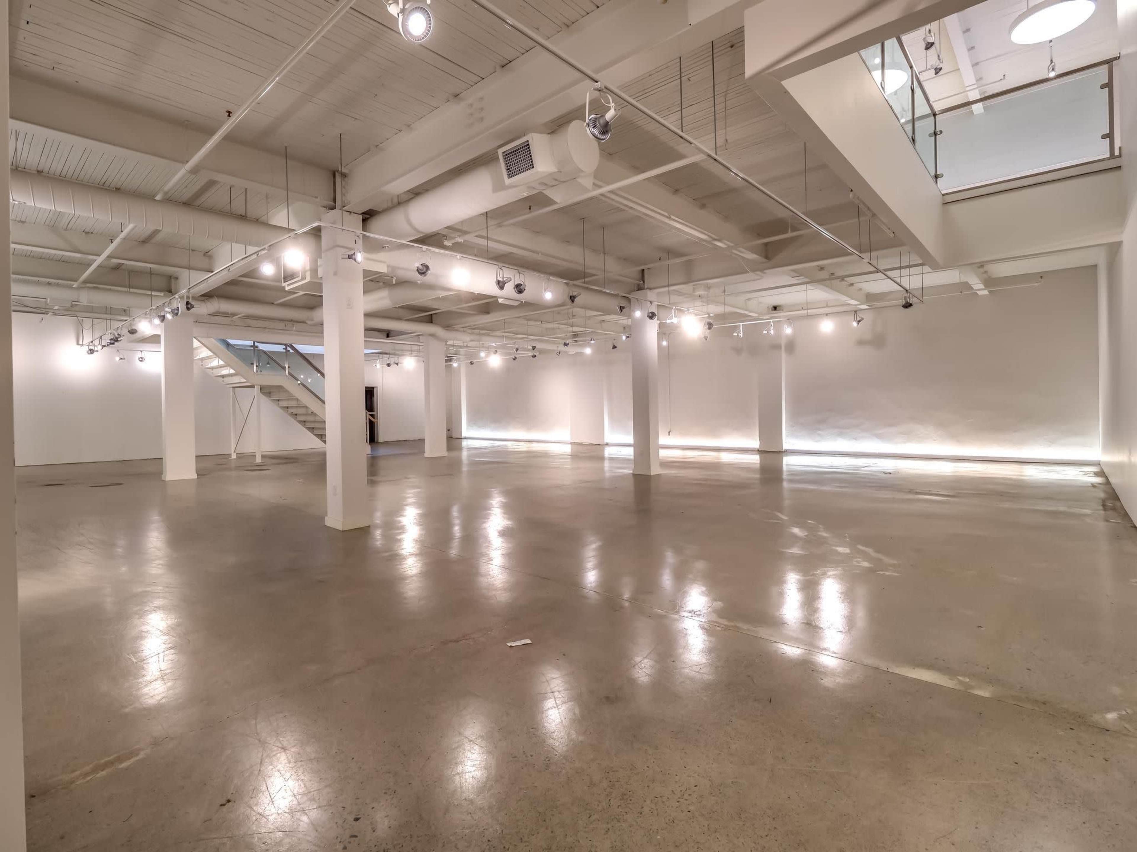 A spacious, minimally furnished interior with concrete flooring and white walls, illuminated by overhead lights.