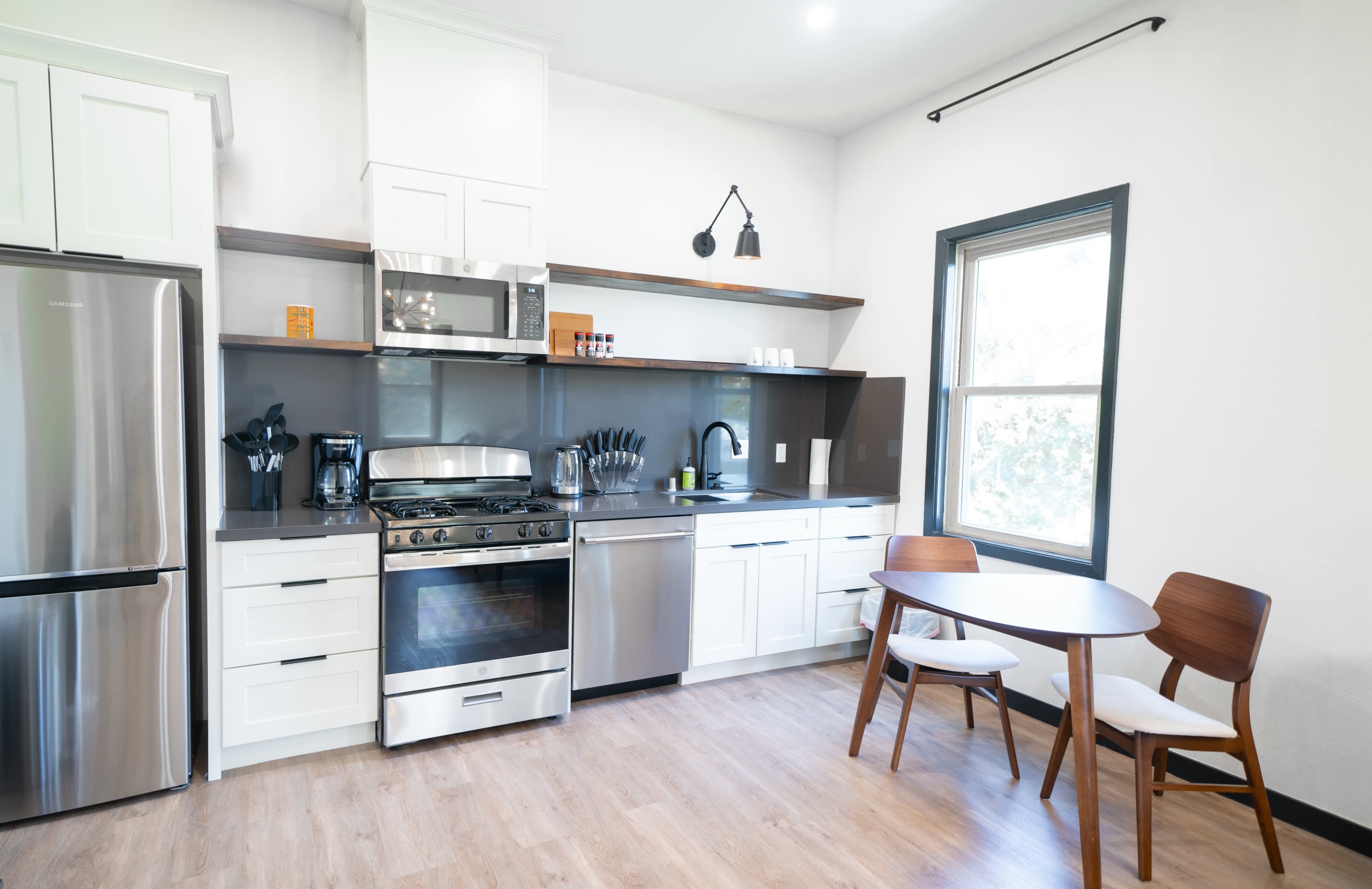 A modern kitchen with stainless steel appliances, white cabinetry, and a circular wooden dining table with two chairs.