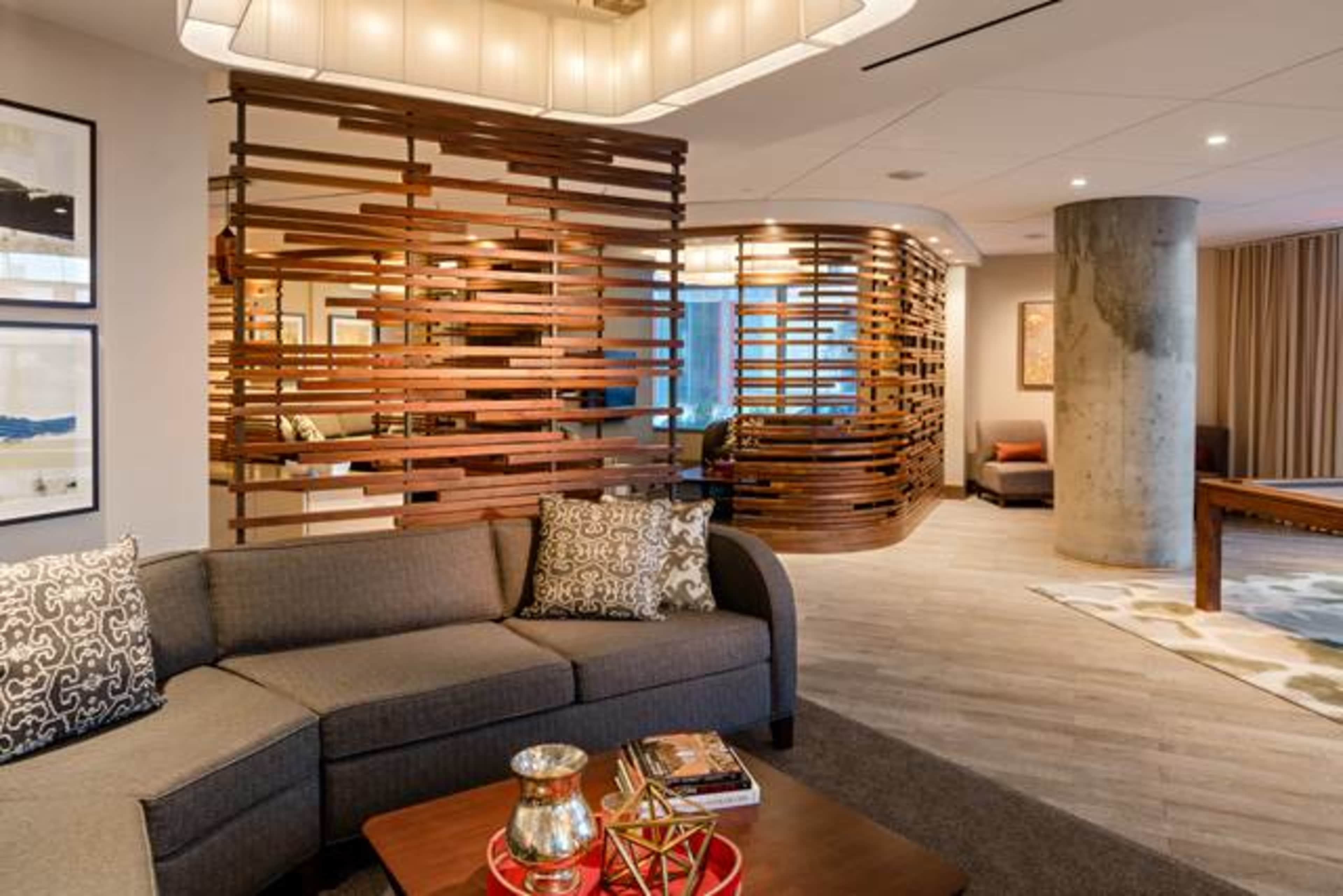 A modern lobby area featuring a sectional sofa, a coffee table with decorative items, and a wooden partition creating a separate space.