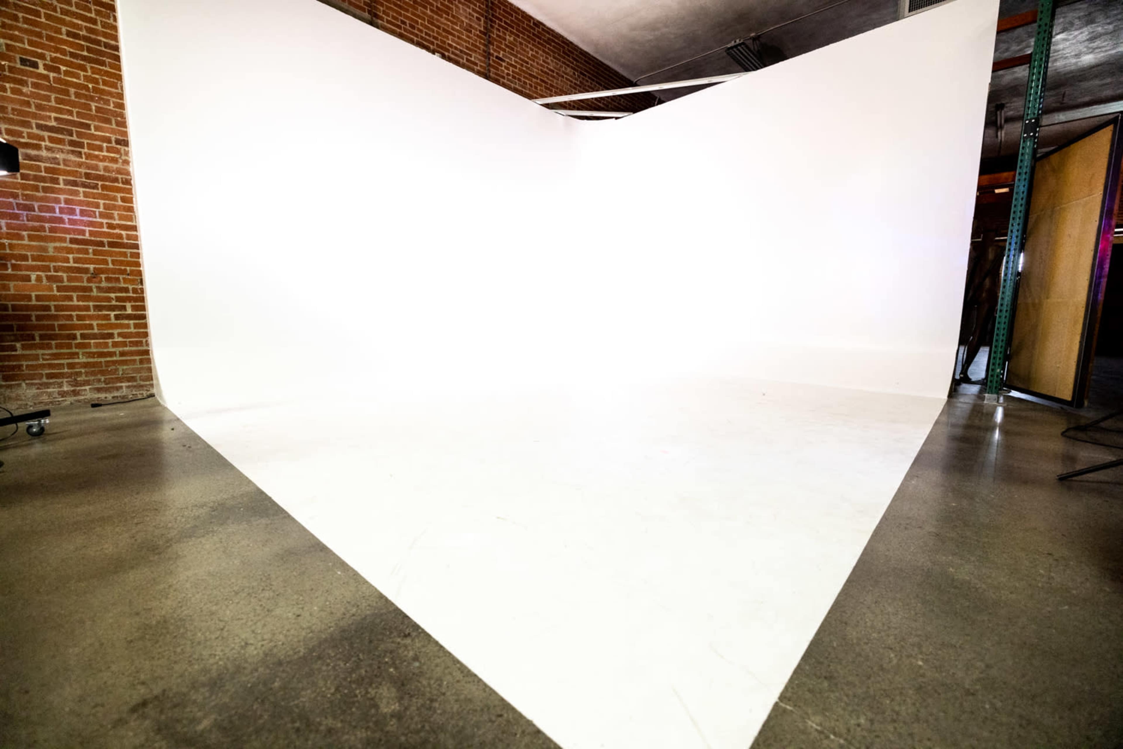 A spacious studio features a large, white backdrop meeting the floor at a sharp angle.