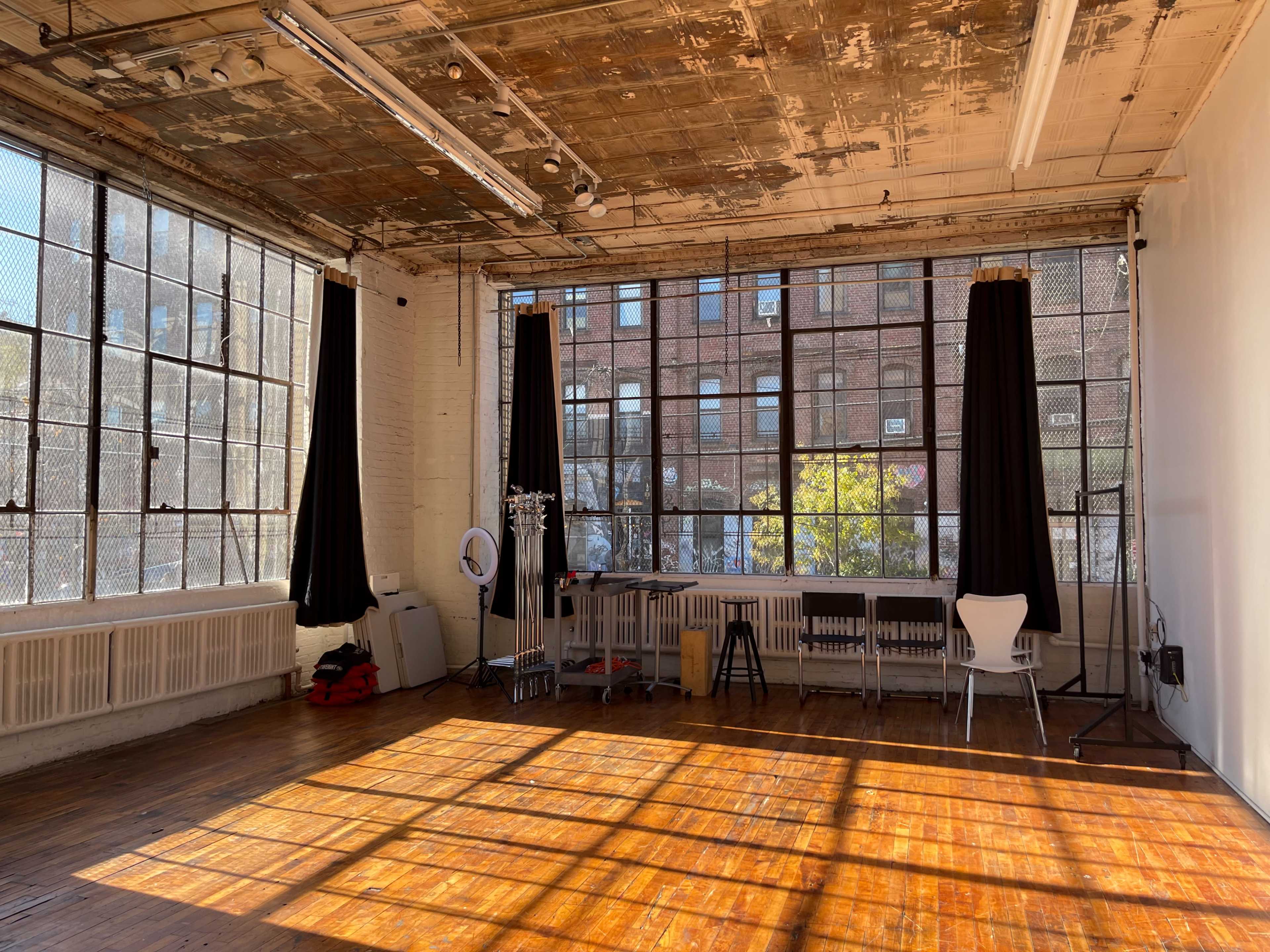 A spacious, sunlit room with large windows, wooden floors, and black curtains.