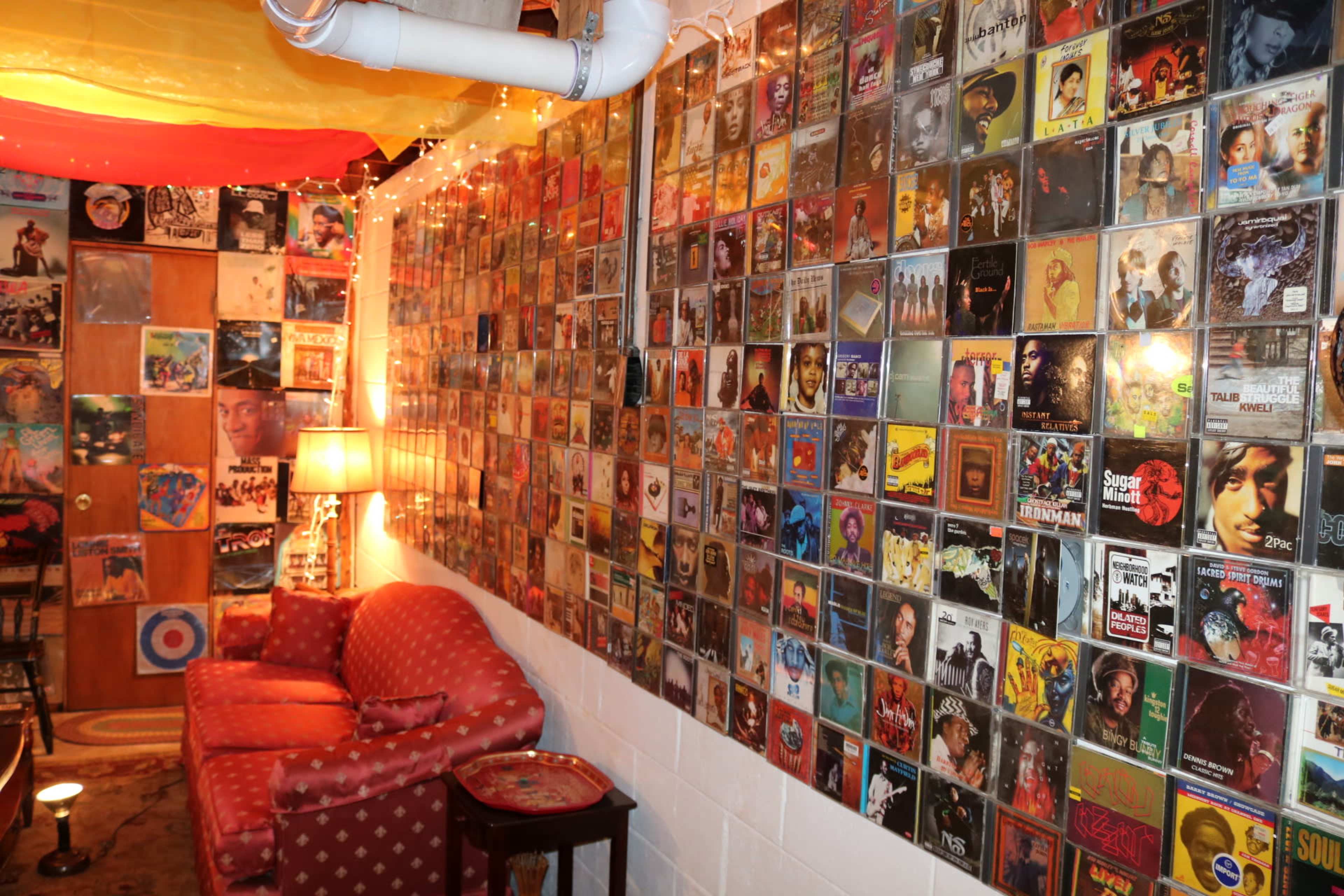 A cozy room with a wall covered in framed album covers, beside a red polka-dotted sofa and a lamp.