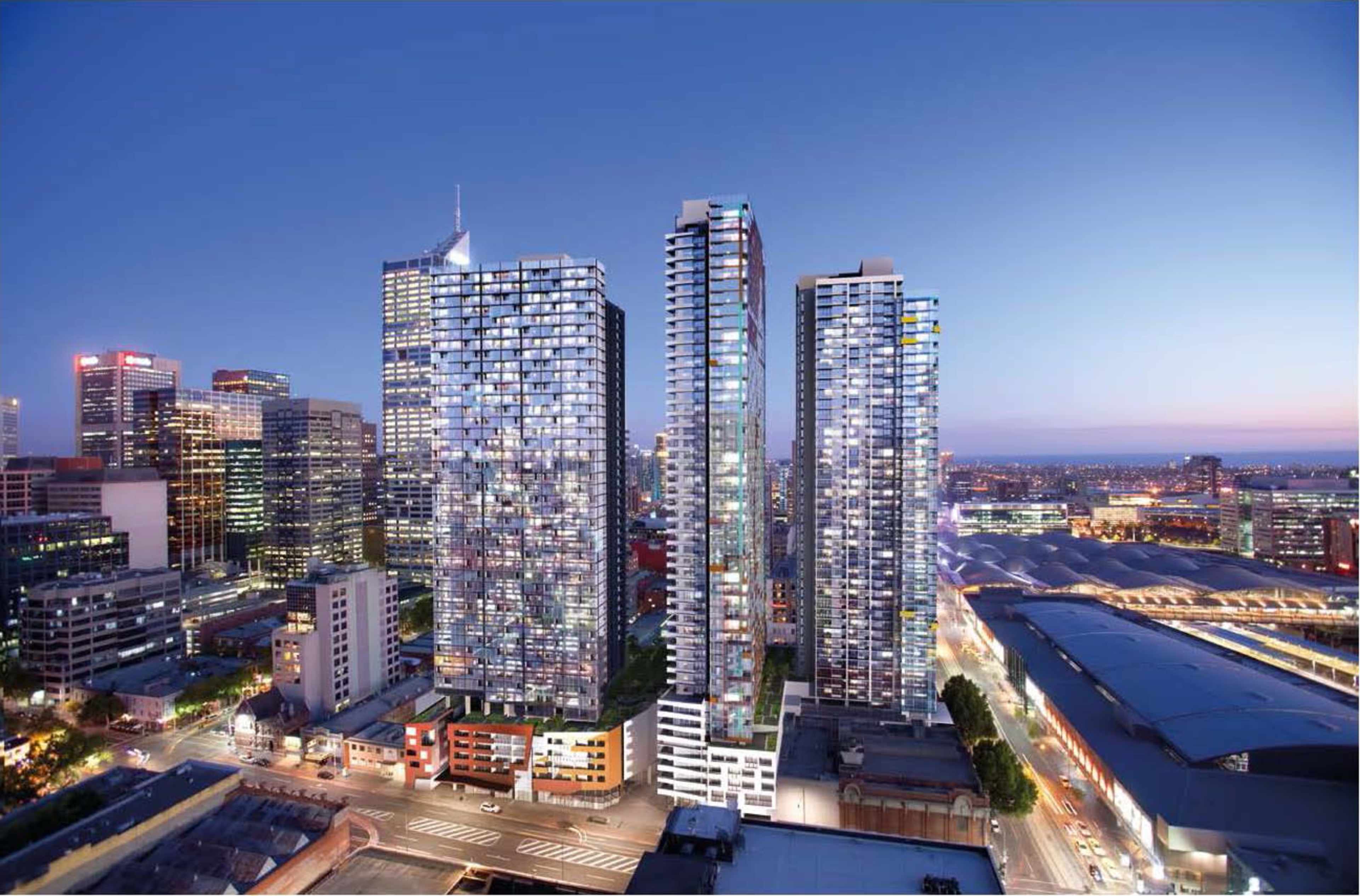 A city skyline at dusk with three modern high-rise buildings illuminated against the backdrop of a blue sky.