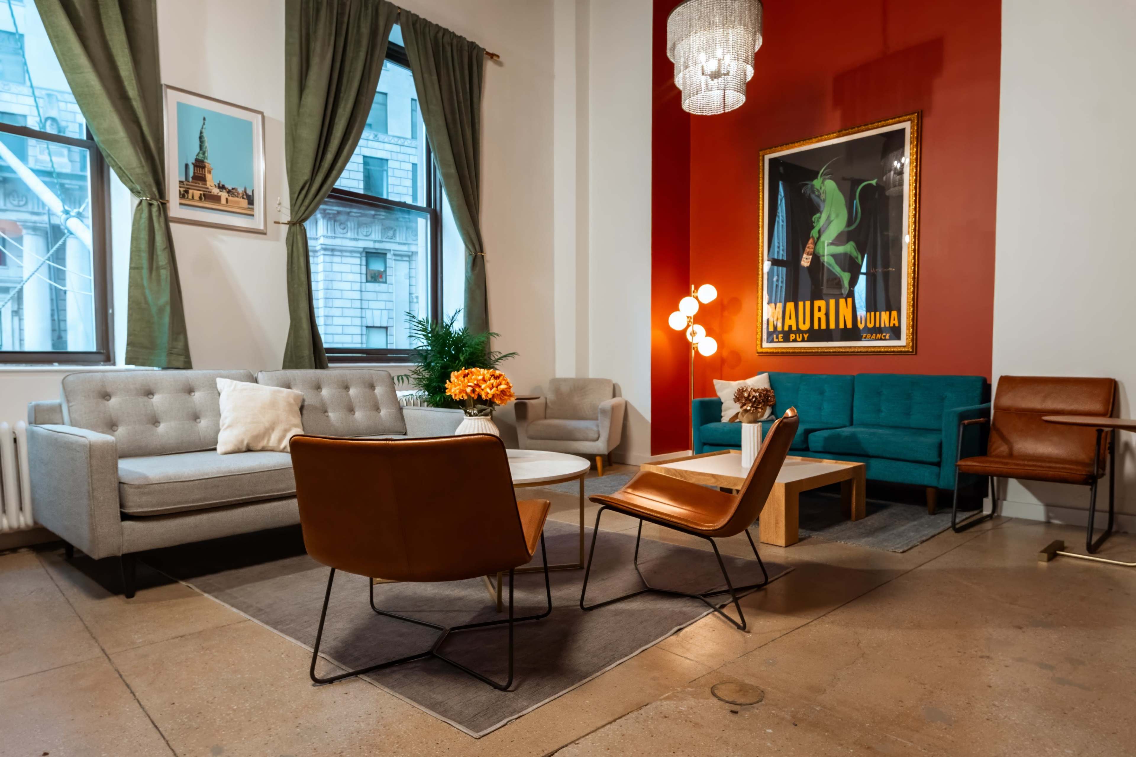 The image shows a modern living room with a mix of seating options, including a gray sofa, turquoise couch, and leather chairs, set against a vibrant red wall featuring a large framed poster.
